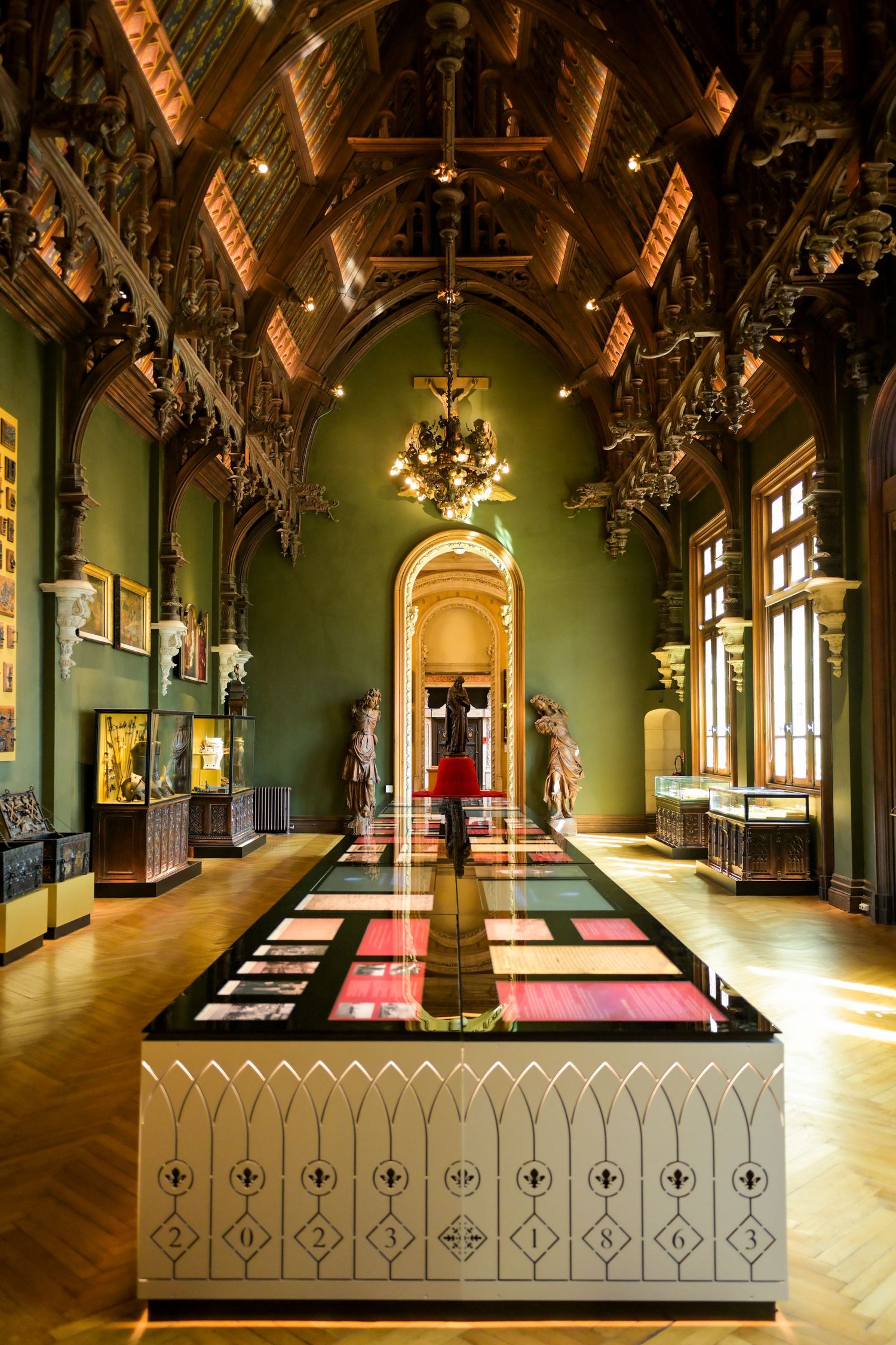 Ornate gothic hall with green walls, wooden beams, and dramatic lighting displaying museum exhibits.
