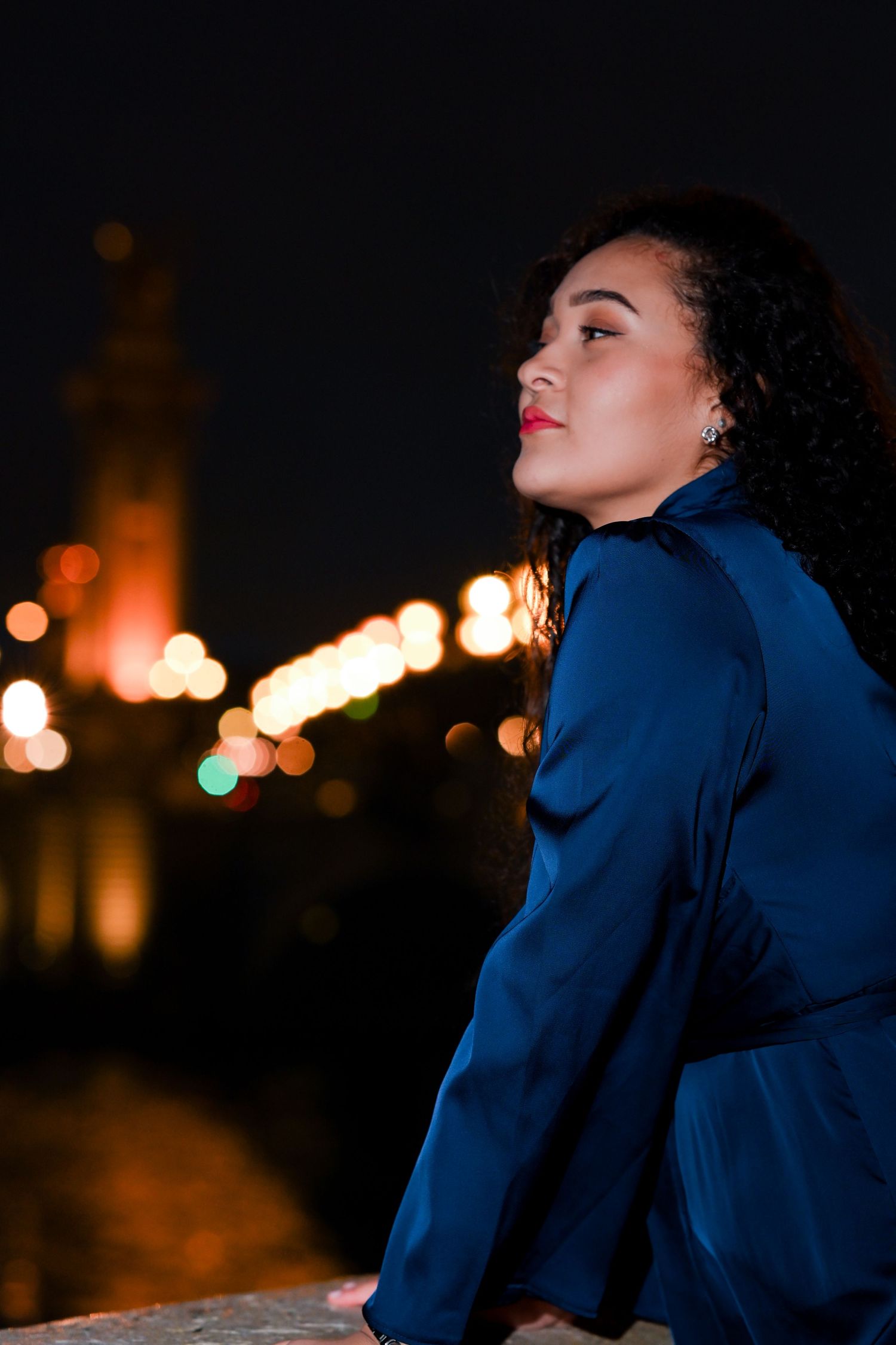 Night portrait with city lights bokeh showing a figure in navy blue against dark background.