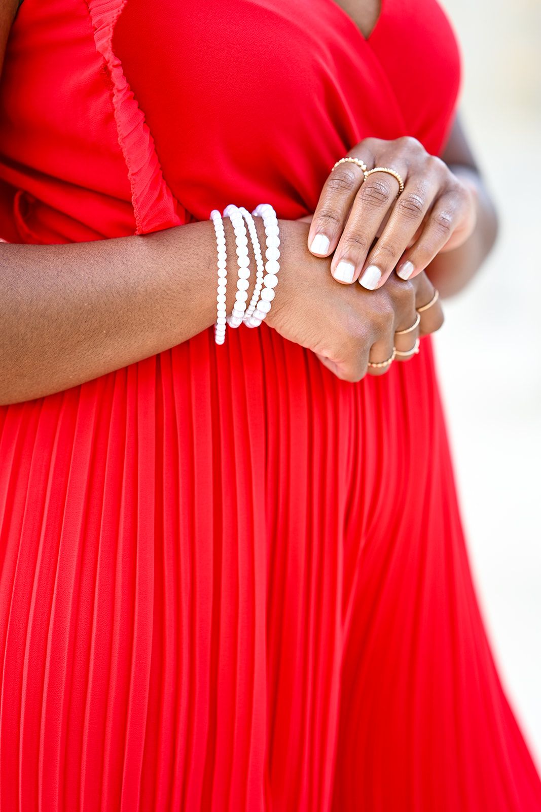 Close-up details of pearl bracelets and rings with red pleated dress fabric.