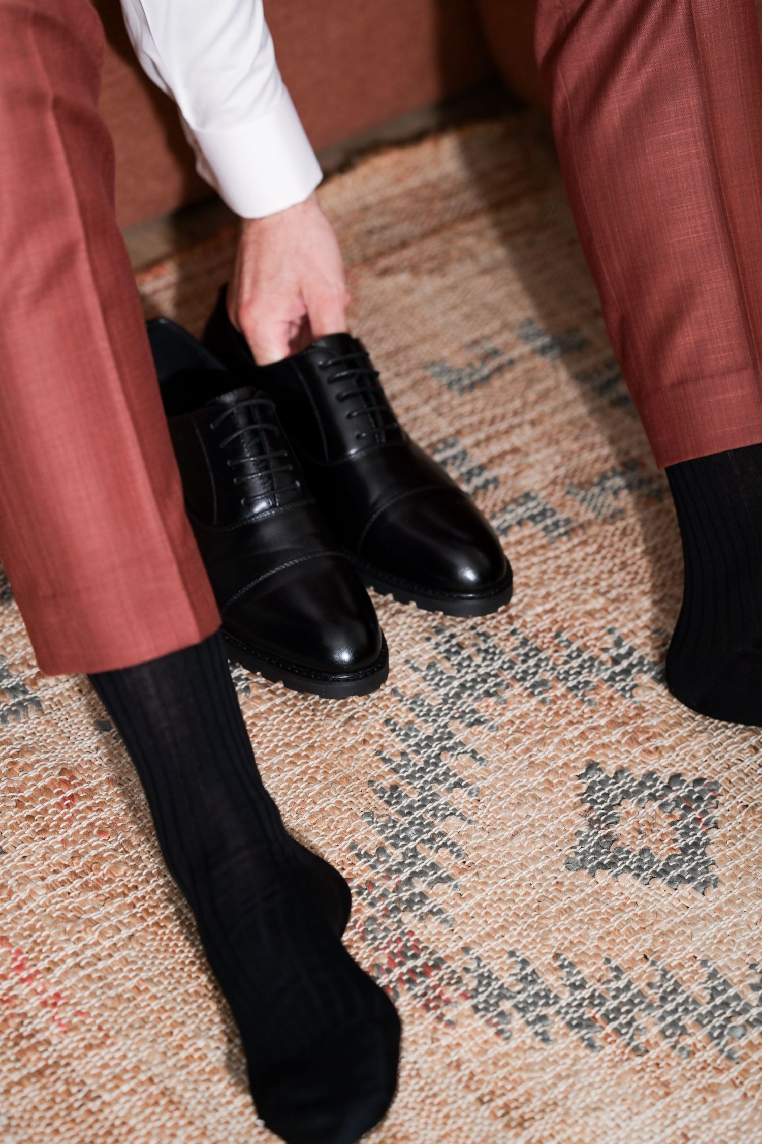 Black dress shoes and socks against a vintage patterned rug.