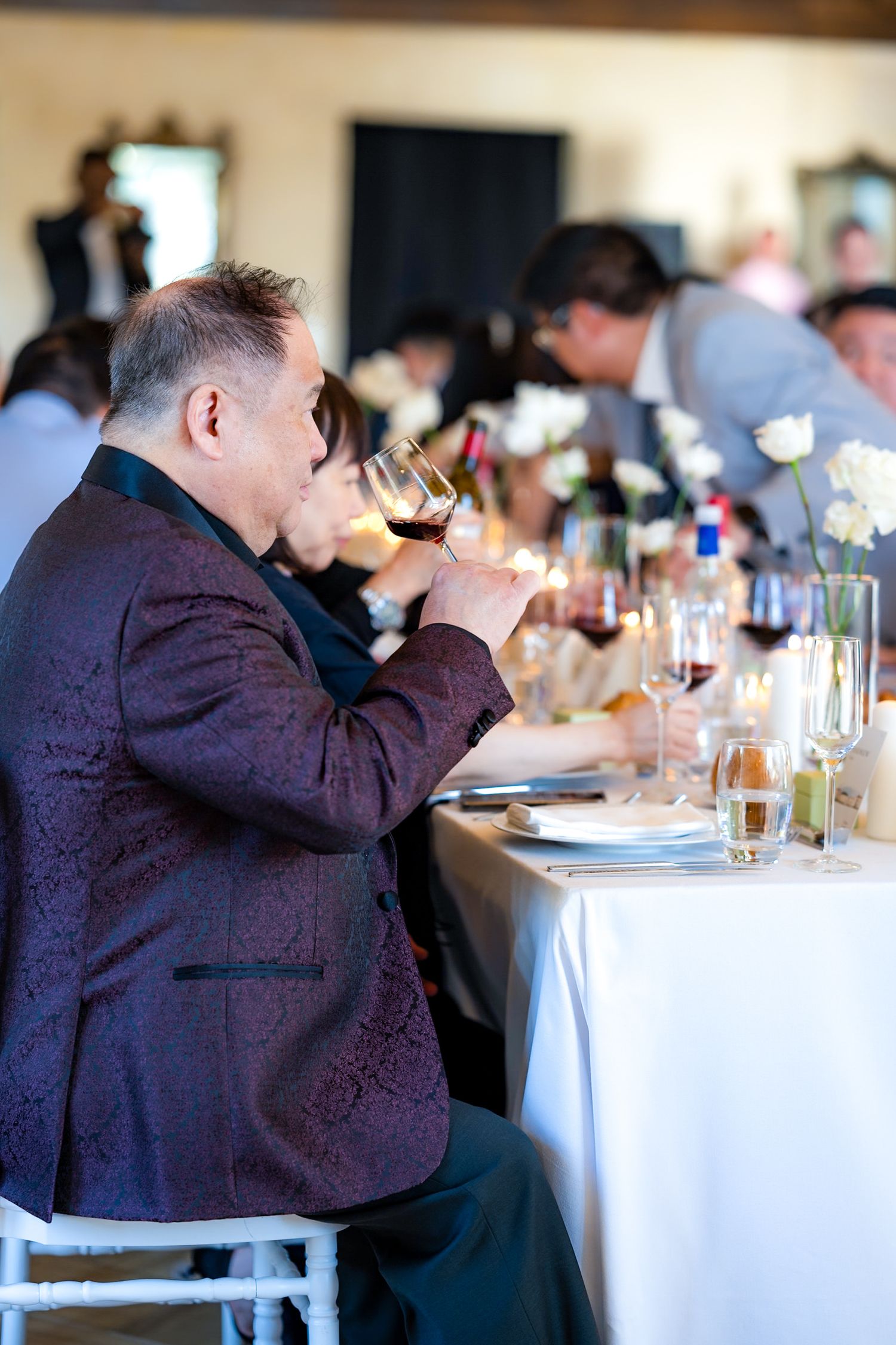 Guest in formal attire sips wine at an elegant dinner table.