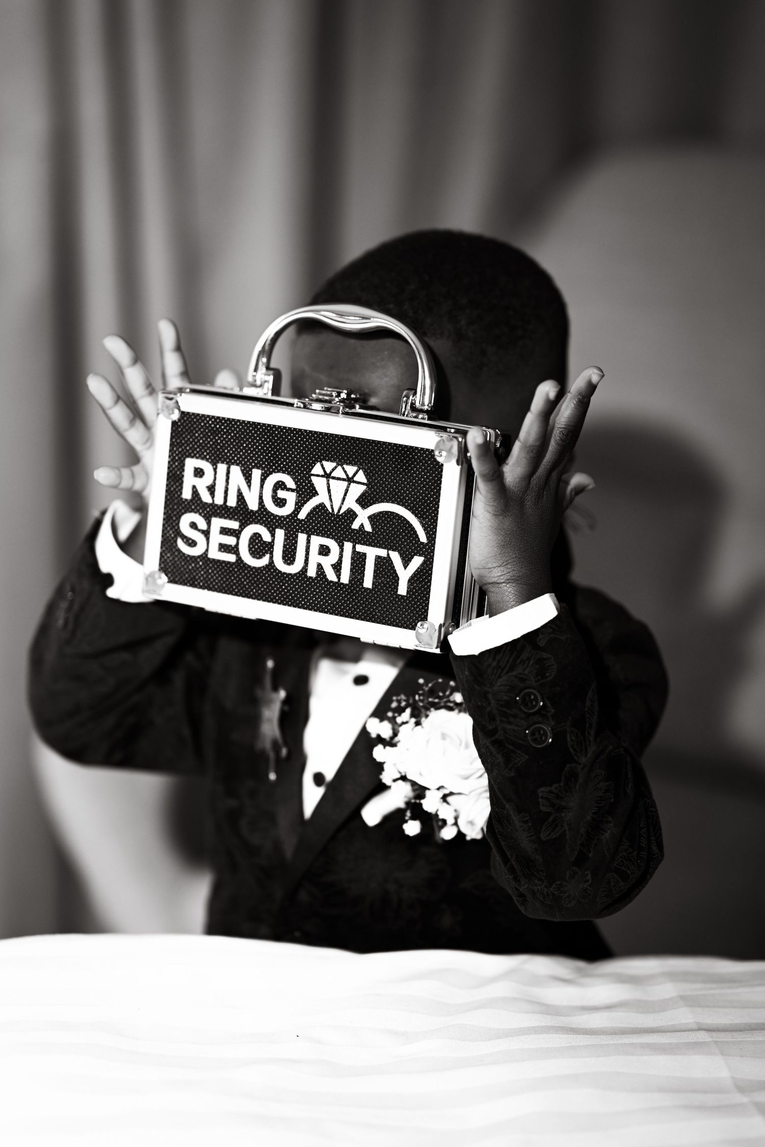 Black and white image of a decorative ring security box displayed on white fabric.