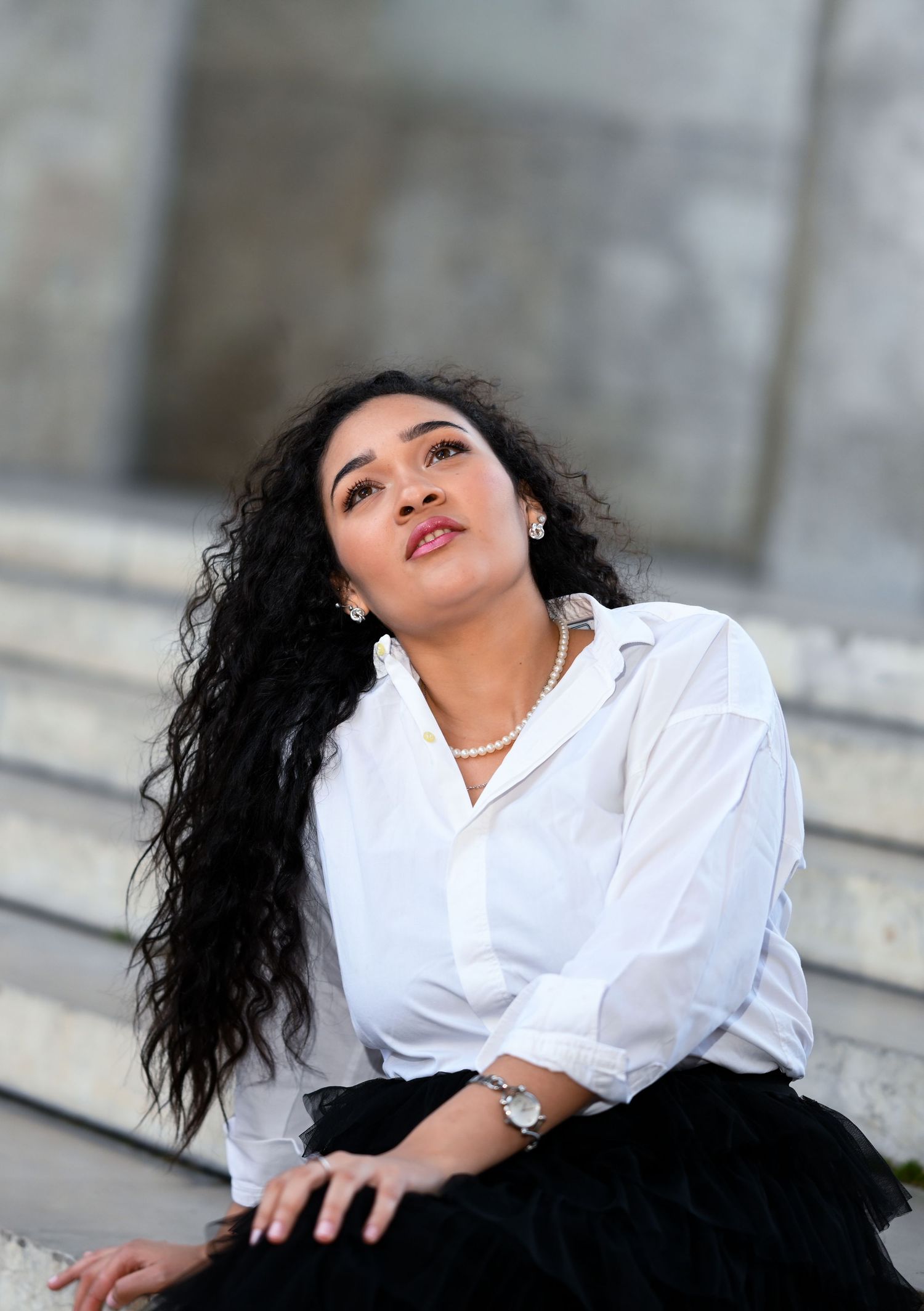 Artistic portrait featuring long curly hair, white blouse and statement jewelry on stone steps.