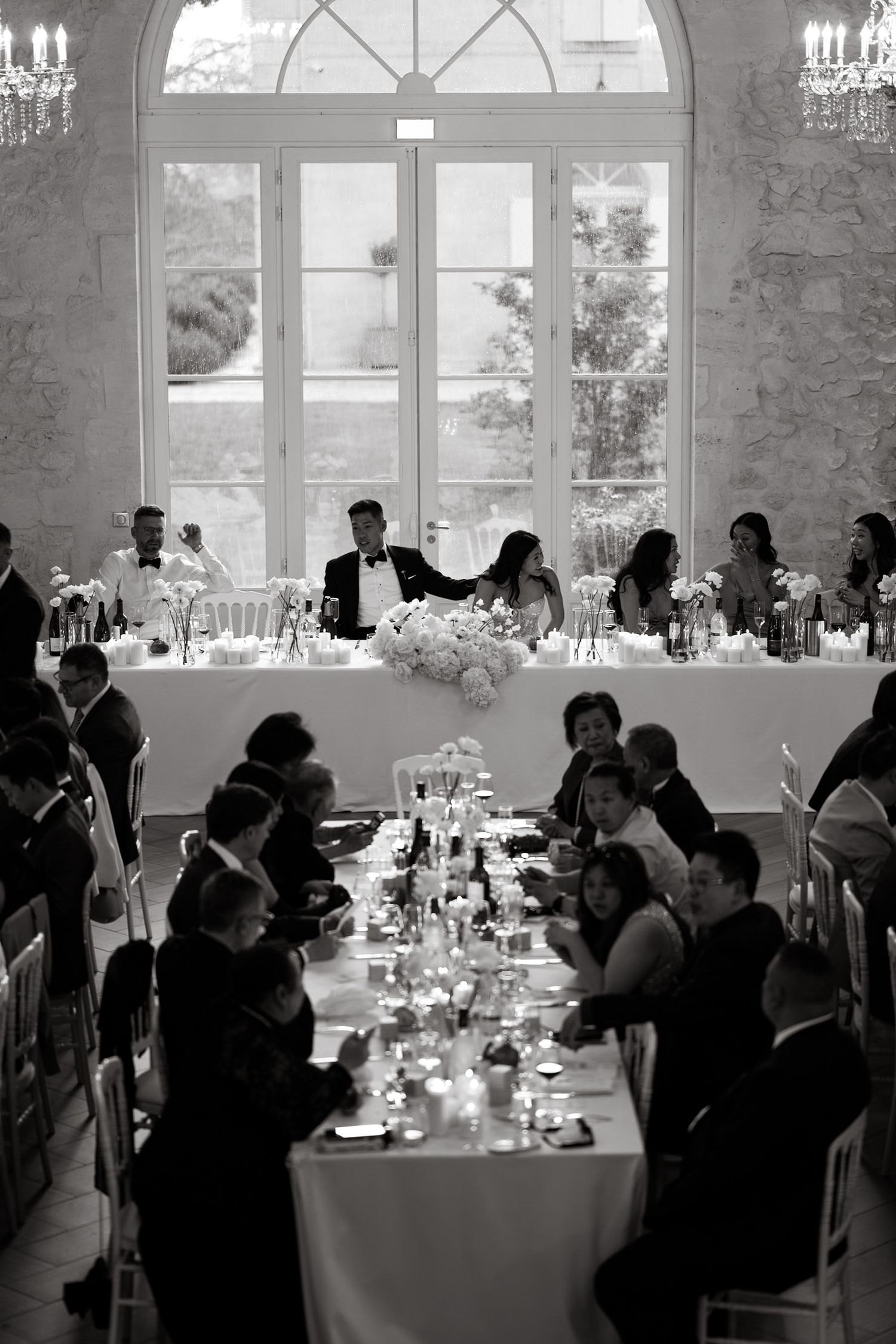 Elegant wedding reception setup with long tables and arched windows in a stone-walled venue.