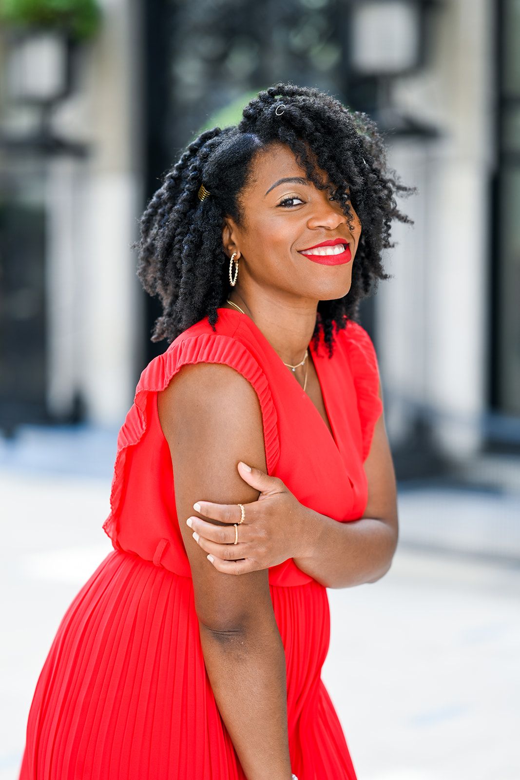 Joyful fashion poses in bright red dress against urban backdrop.