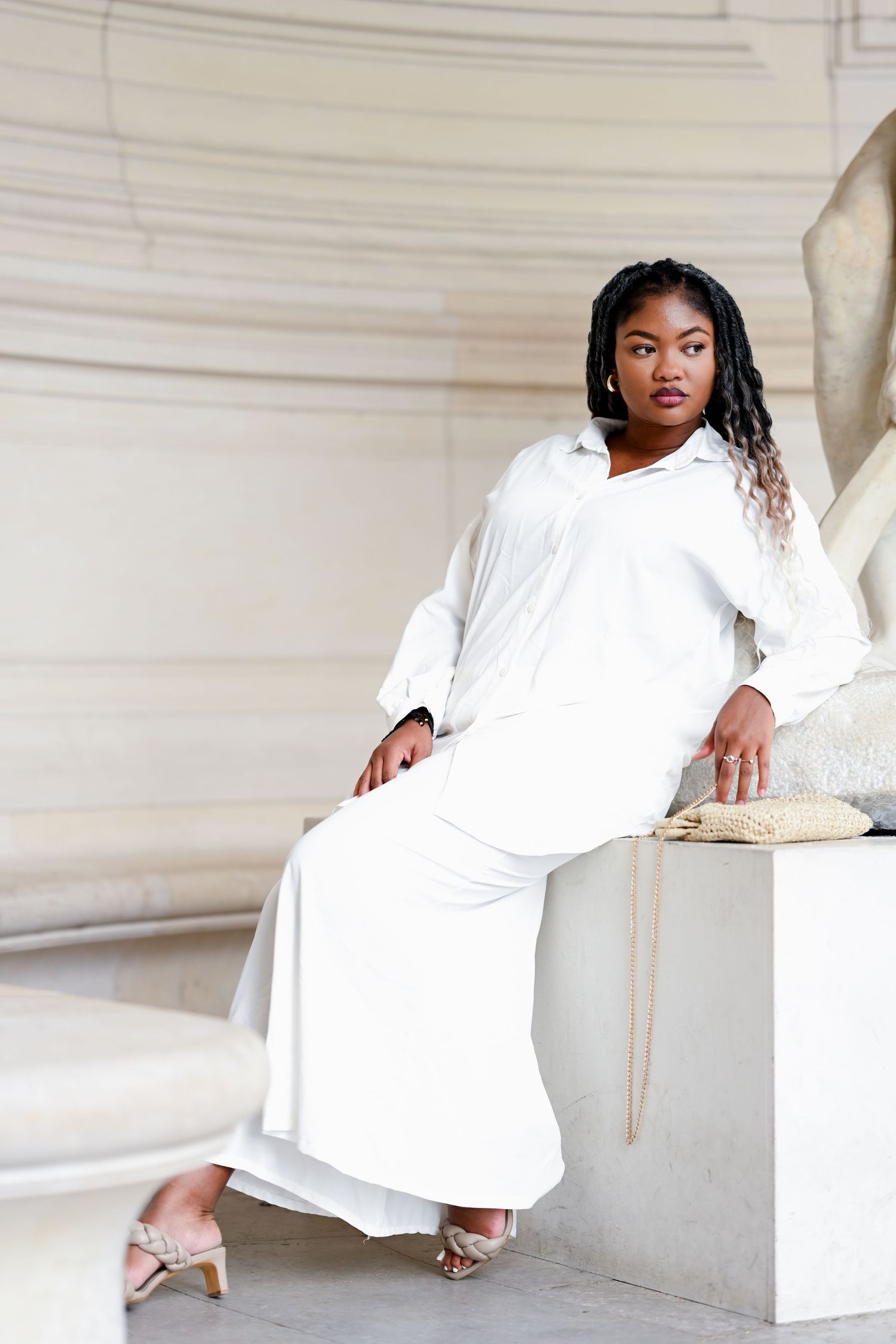 Woman in white dress poses gracefully in minimalist setting with architectural elements.