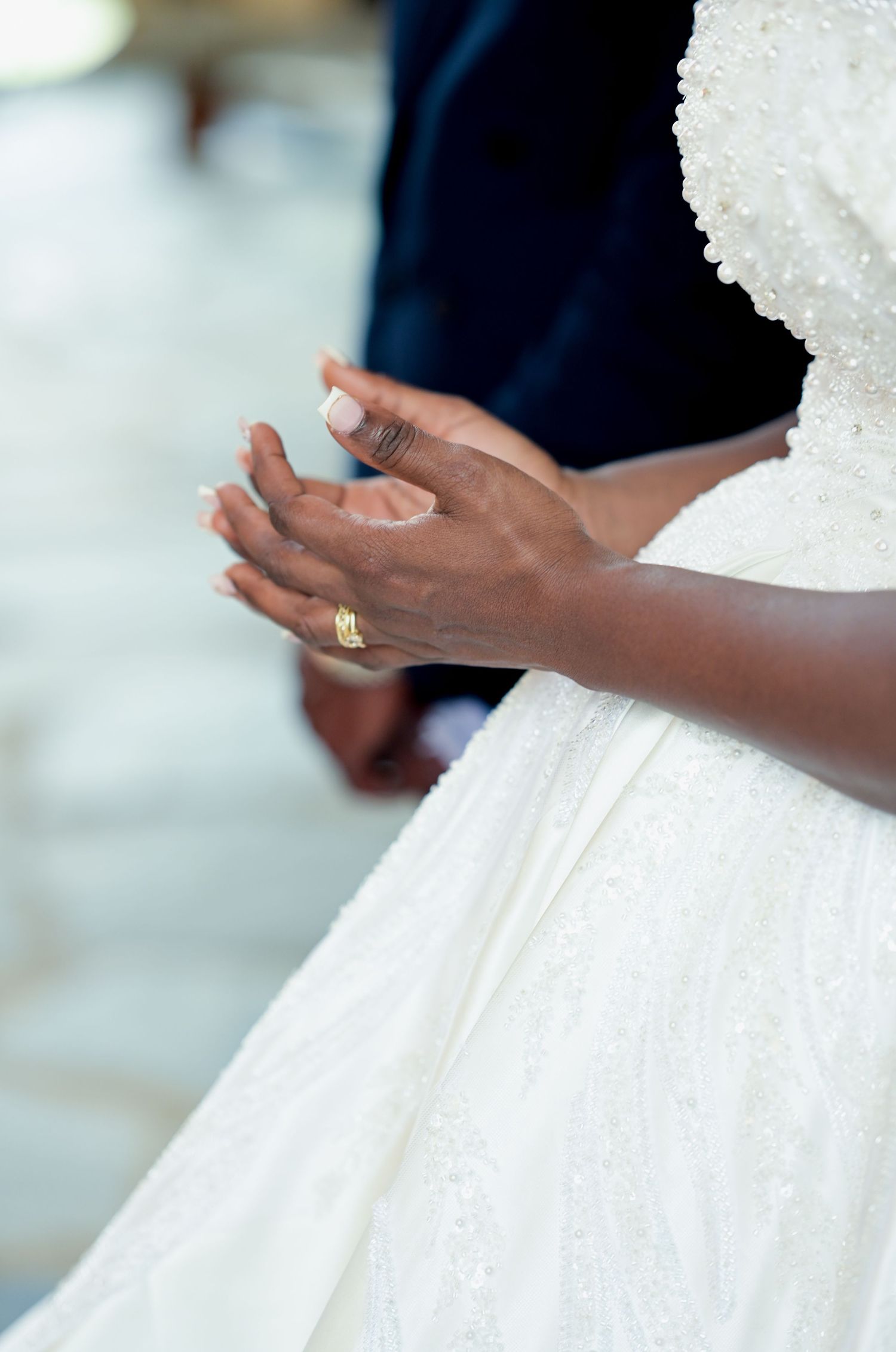Close-up details of a white beaded wedding dress and hands with rings.