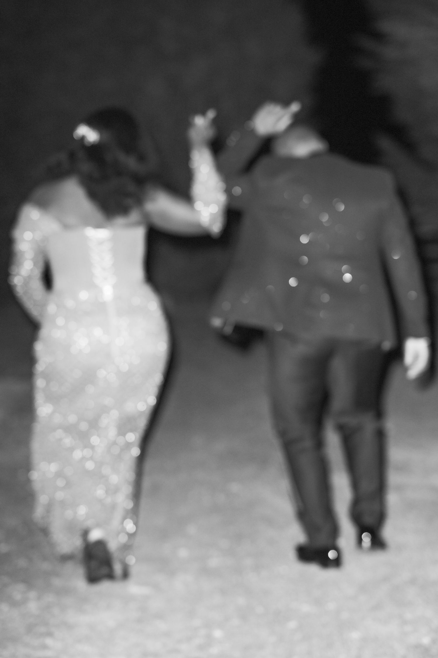 Blurred black and white photo of a couple walking together in formal attire.