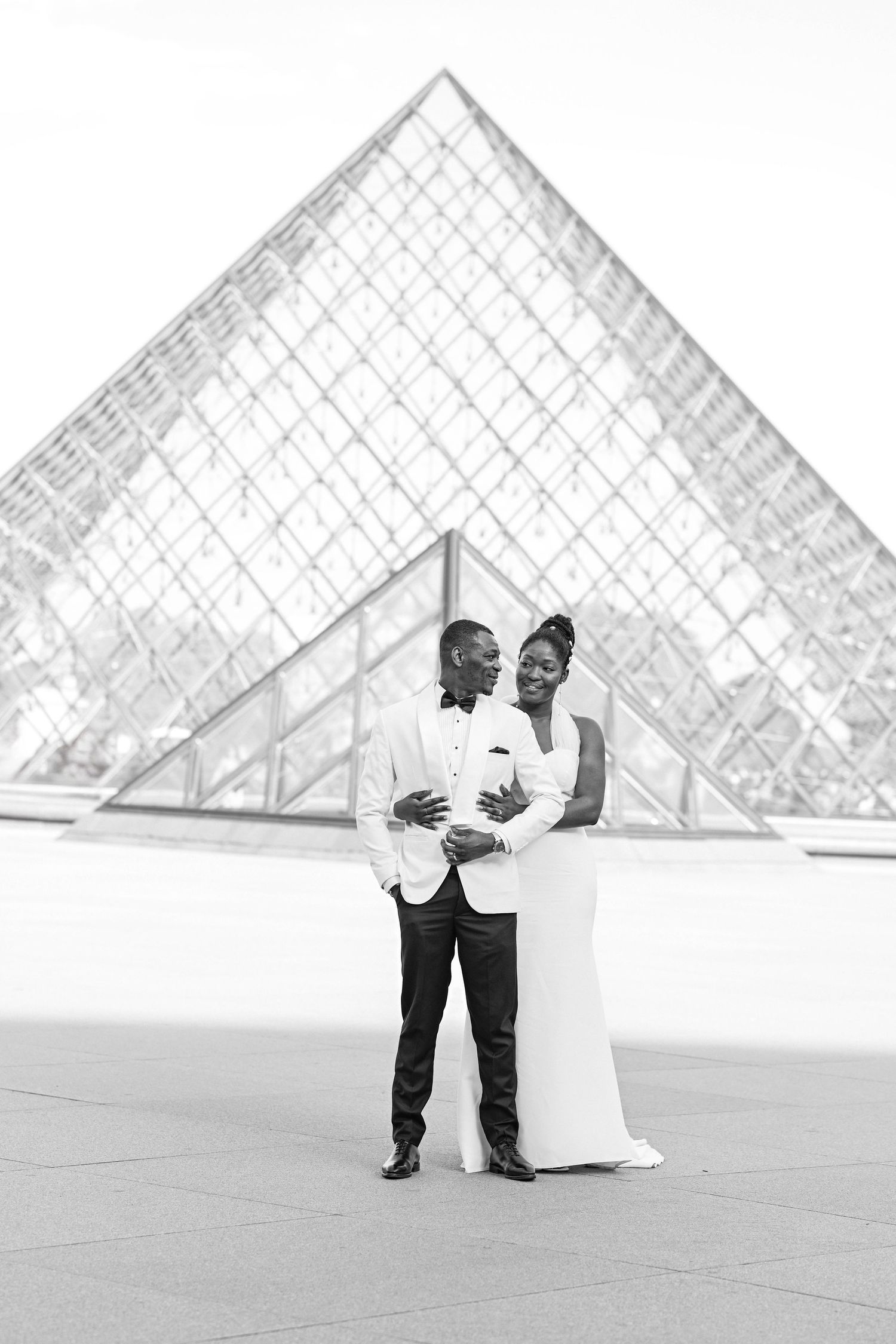 Romantic wedding photoshoot in front of the iconic glass pyramid at the Louvre Museum in Paris.