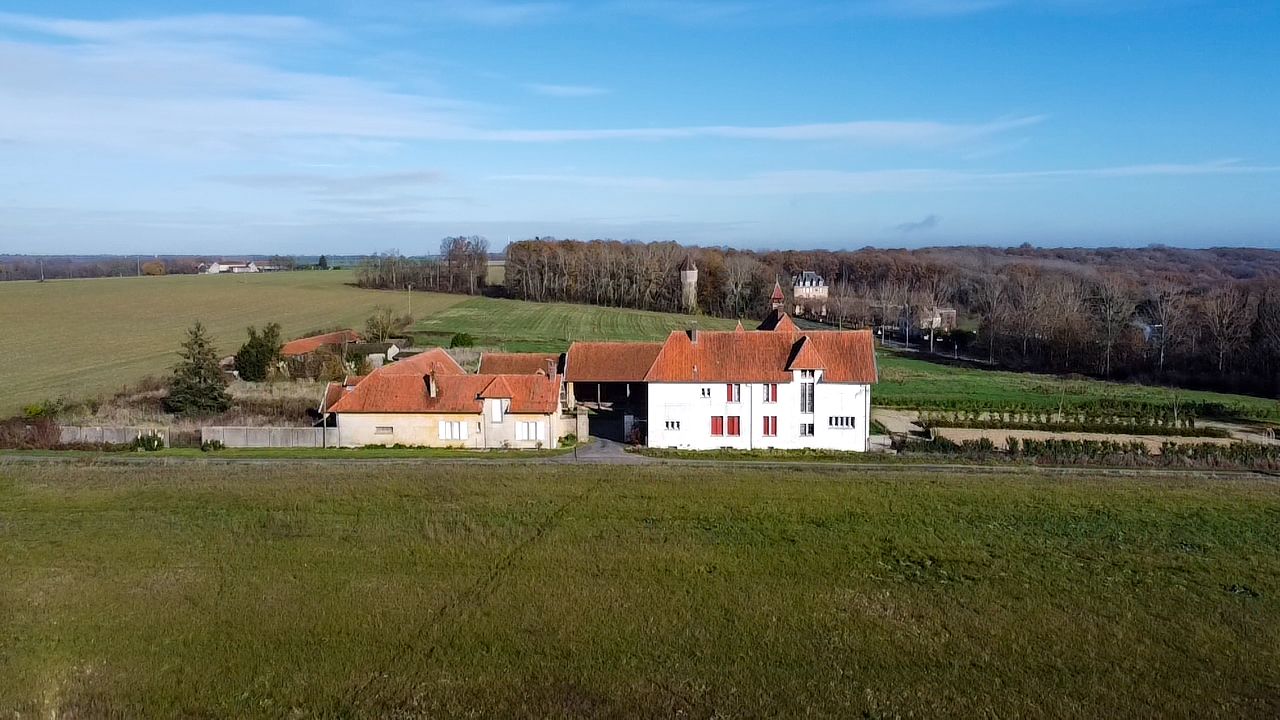 Aerial view of a white farmhouse with red roof surrounded by green fields and trees.