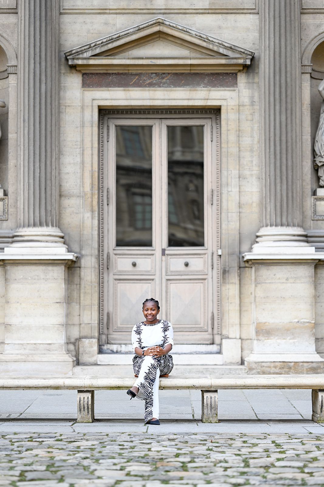 Two people pose playfully in front of stone columns at a historic building.