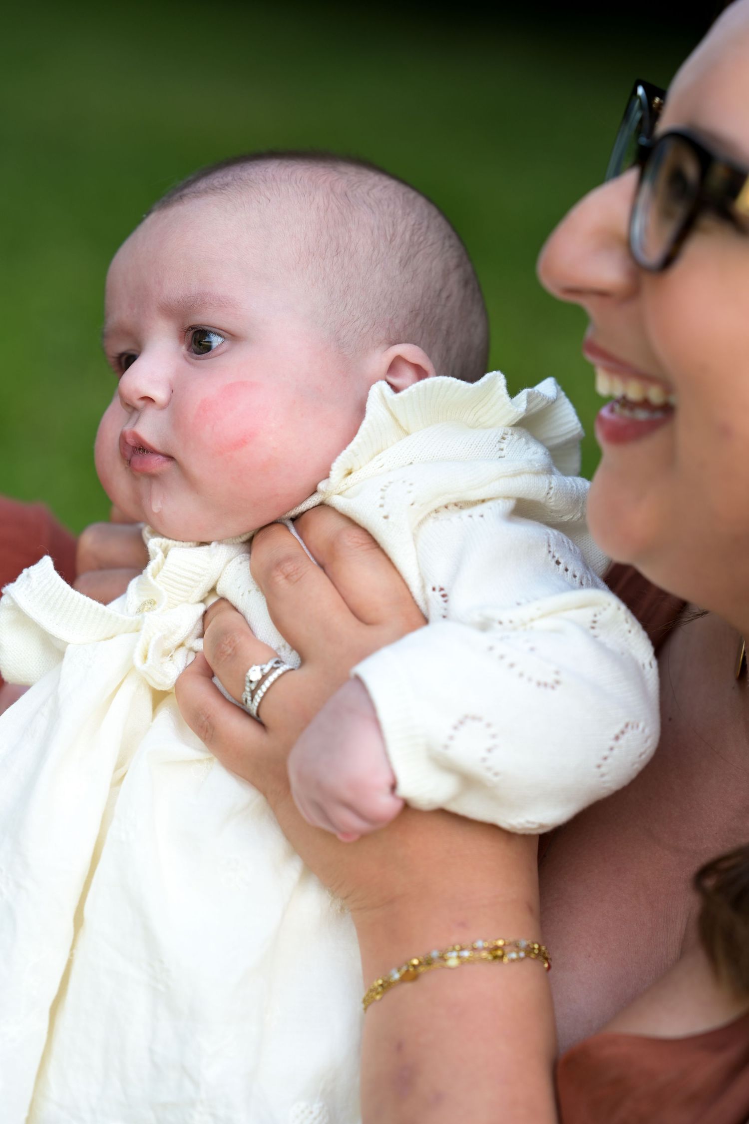 Close-up of baby in white christening gown with family members.