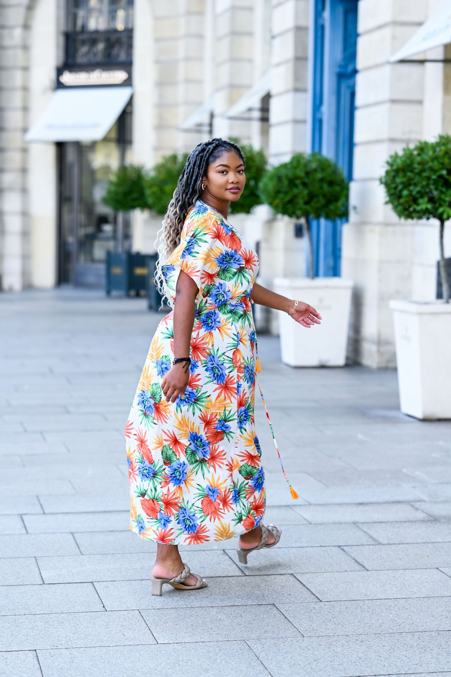 Dynamic fashion poses in tropical print dress against elegant stone colonnade.