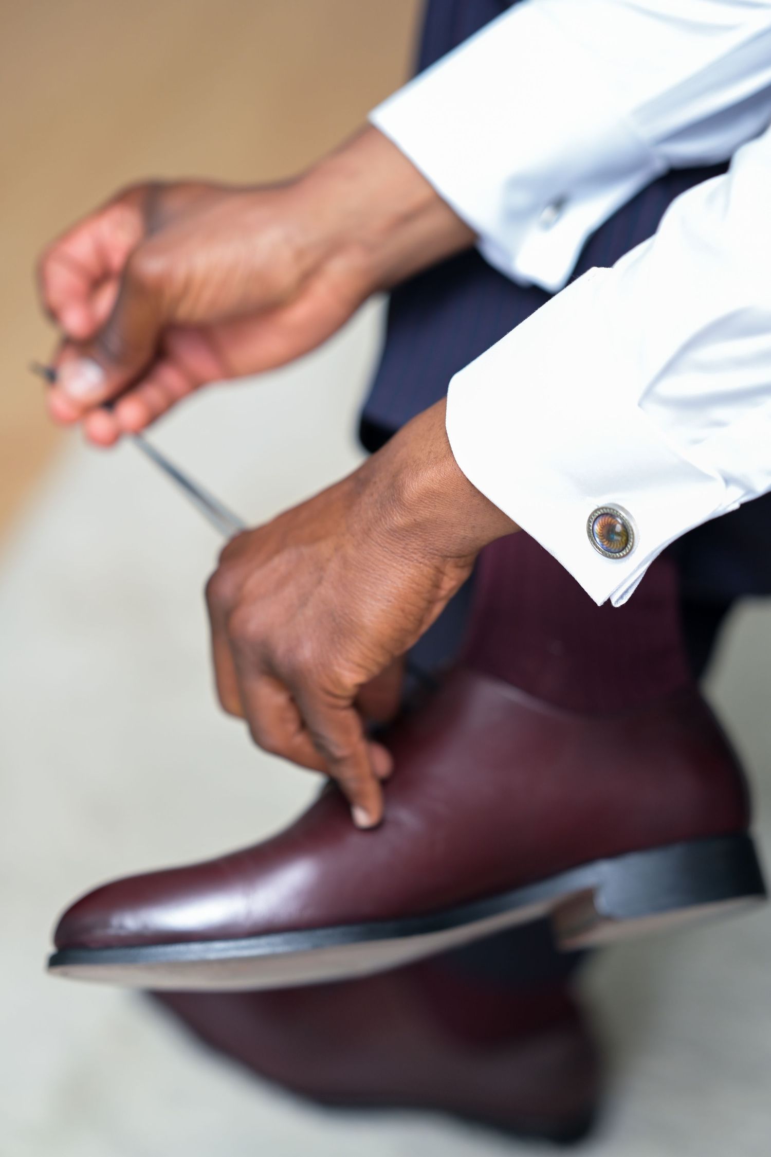 Hands adjusting brown leather dress shoes with white shirt sleeves visible.