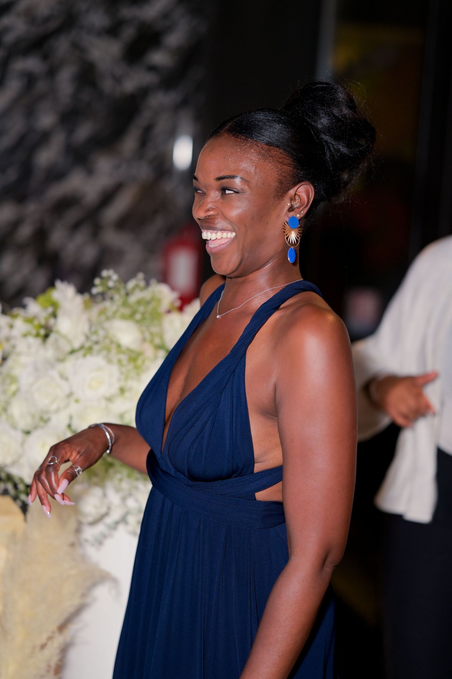A woman in a navy blue dress smiles joyfully at an evening event.