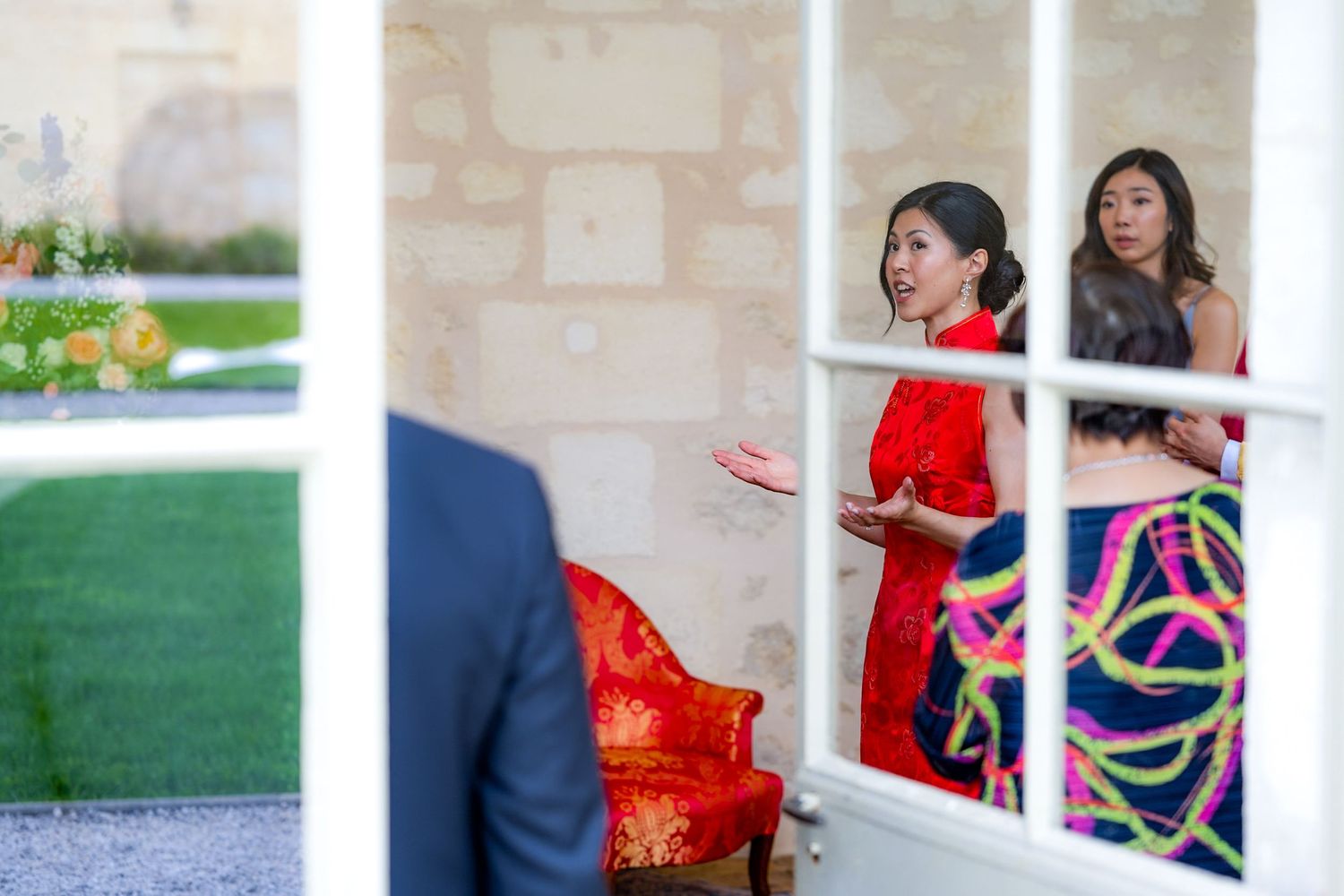 Wedding guests in colorful attire chat through glass doors at an elegant venue.