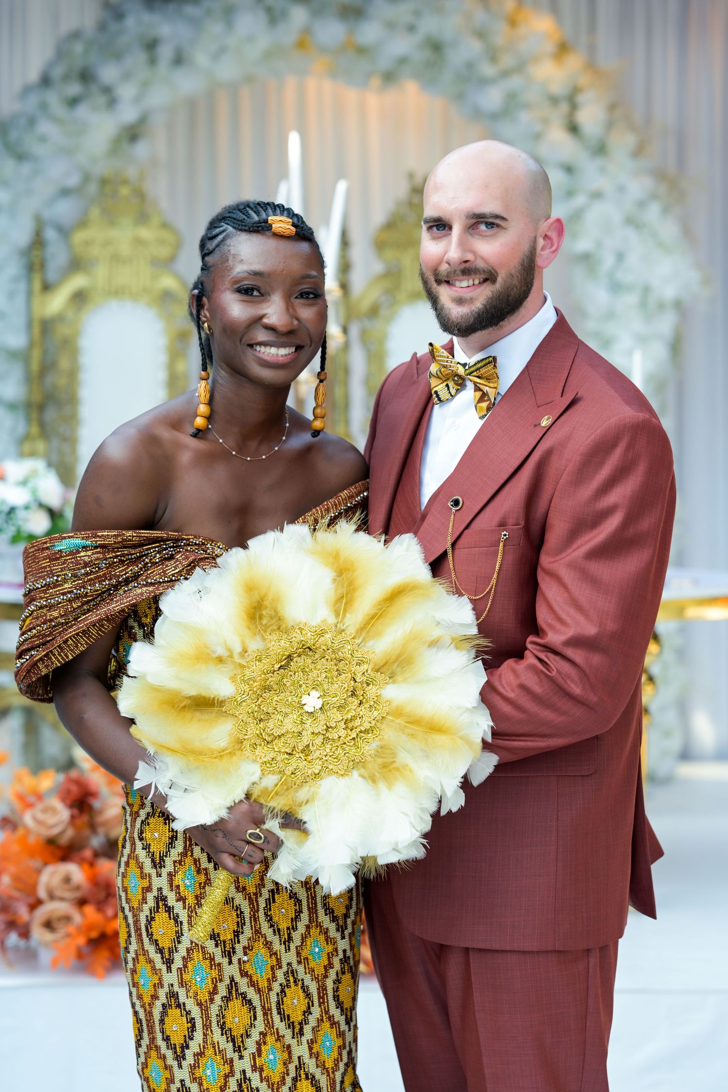 Wedding couple posing with large yellow paper flower decorations against white floral backdrop.