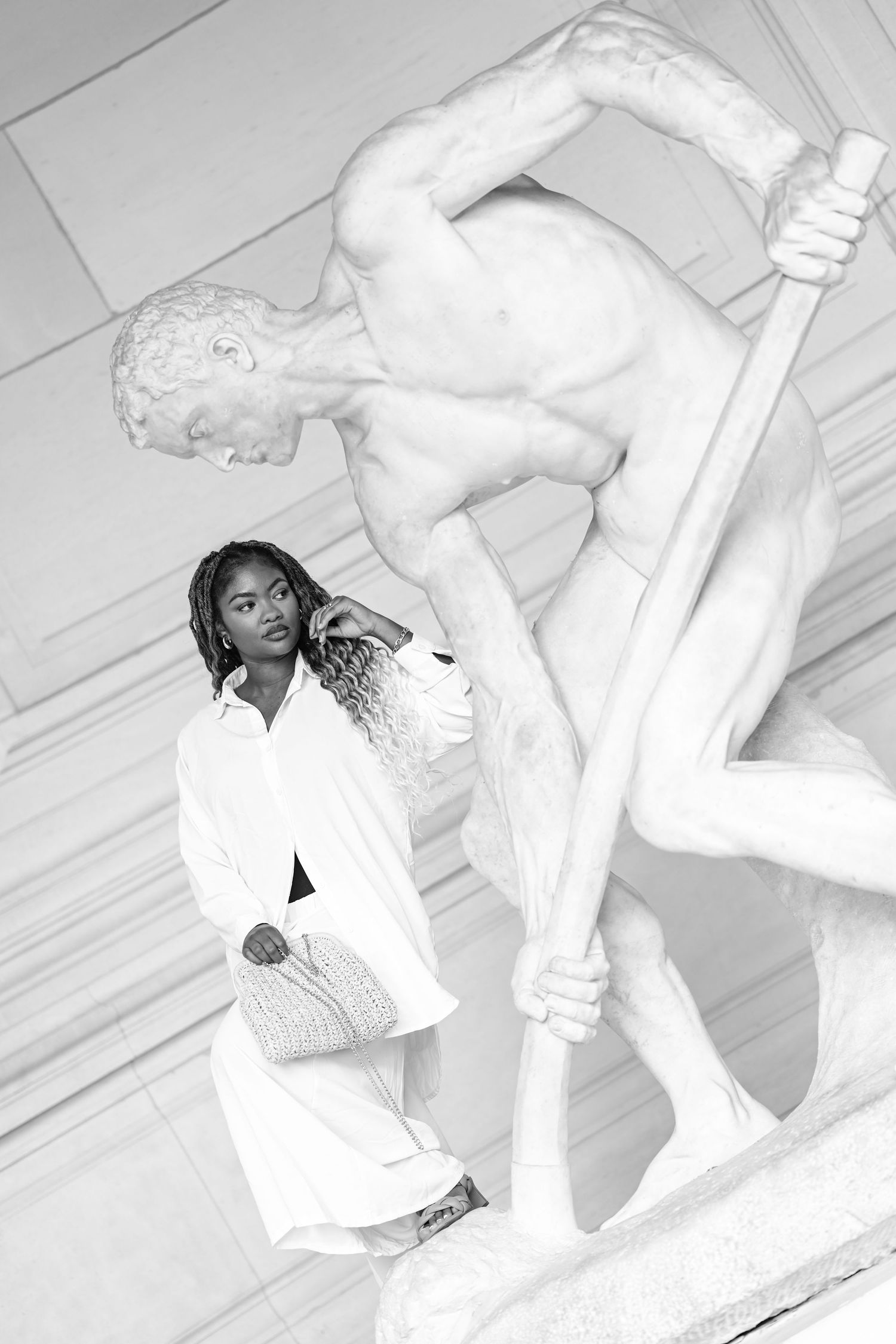 Monochrome fashion photo featuring white outfit against dramatic classical sculpture backdrop.