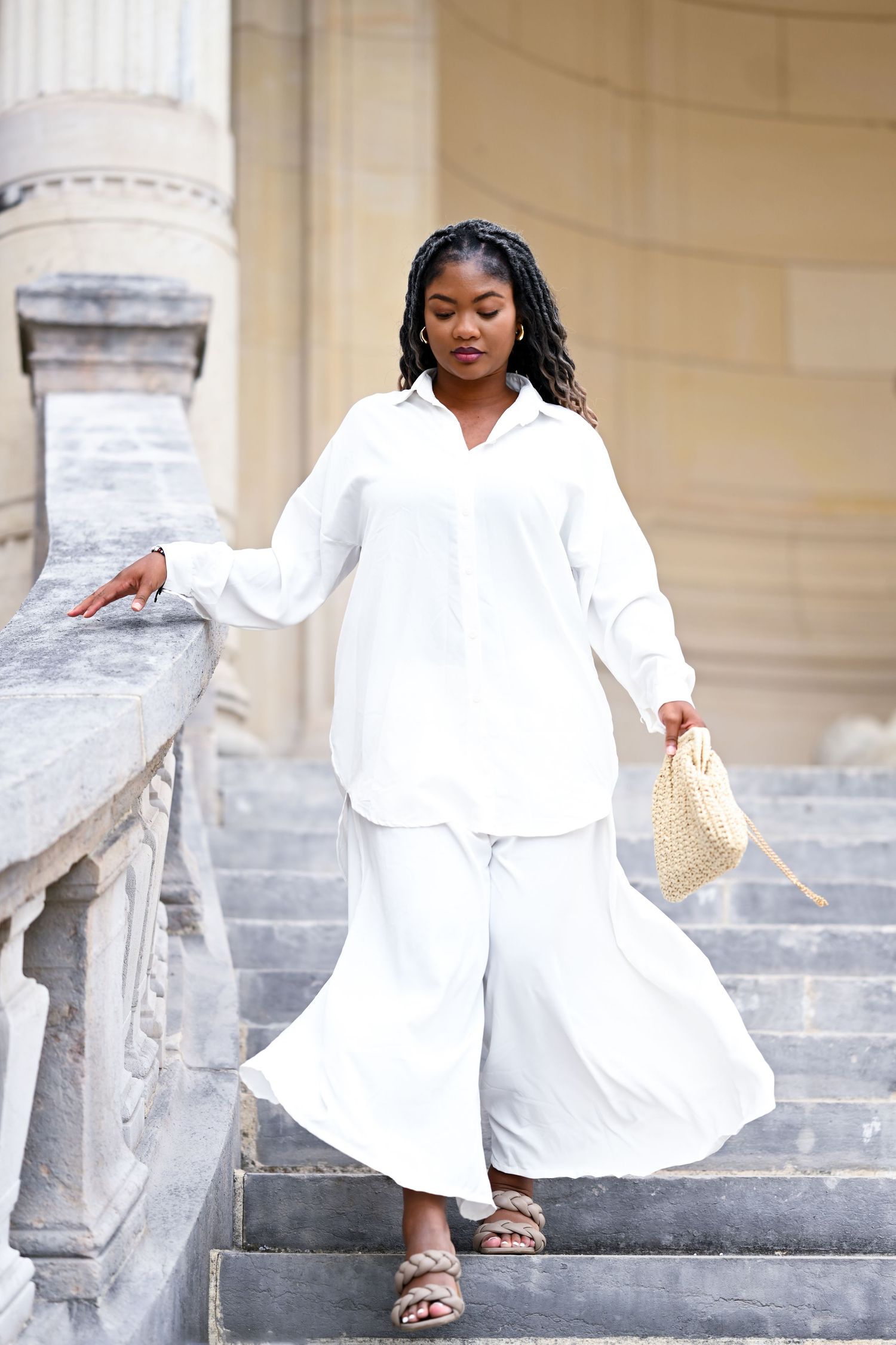Person in white dress poses gracefully on stone steps against classical architecture.