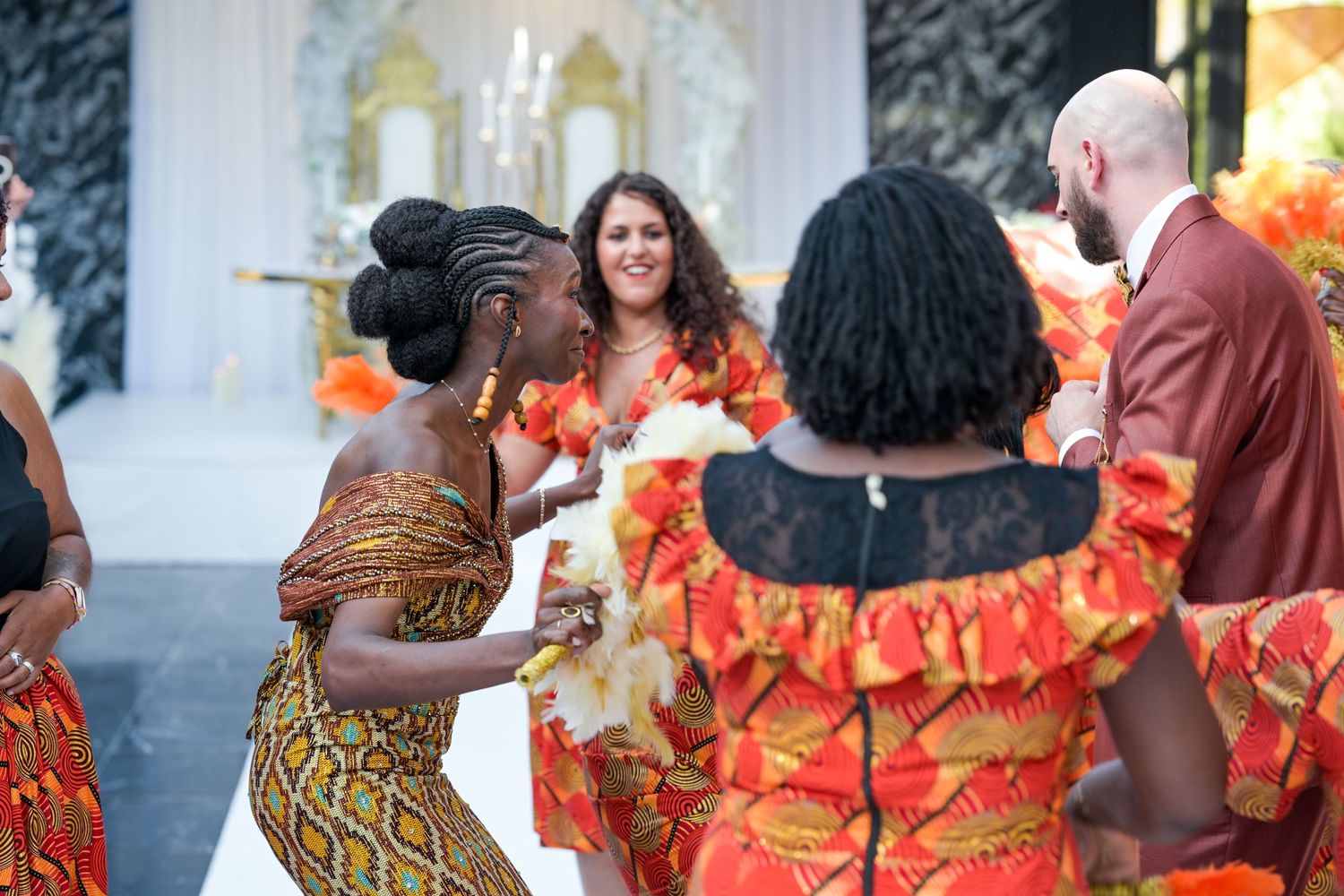 Dancers in vibrant orange and yellow African print dresses perform at a cultural celebration.