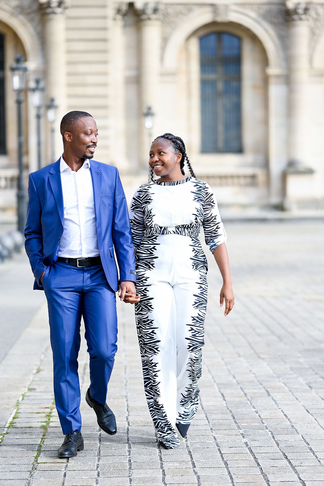 A couple walks hand in hand on cobblestone pavement wearing coordinated outfits.