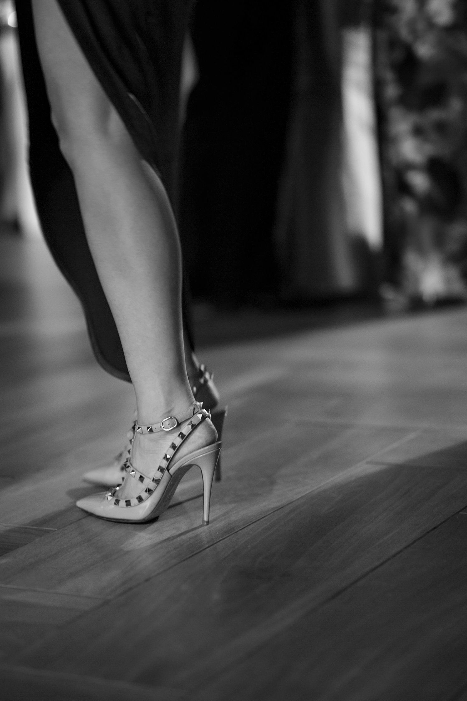 Close-up of studded high heel shoe on wooden floor in black and white.