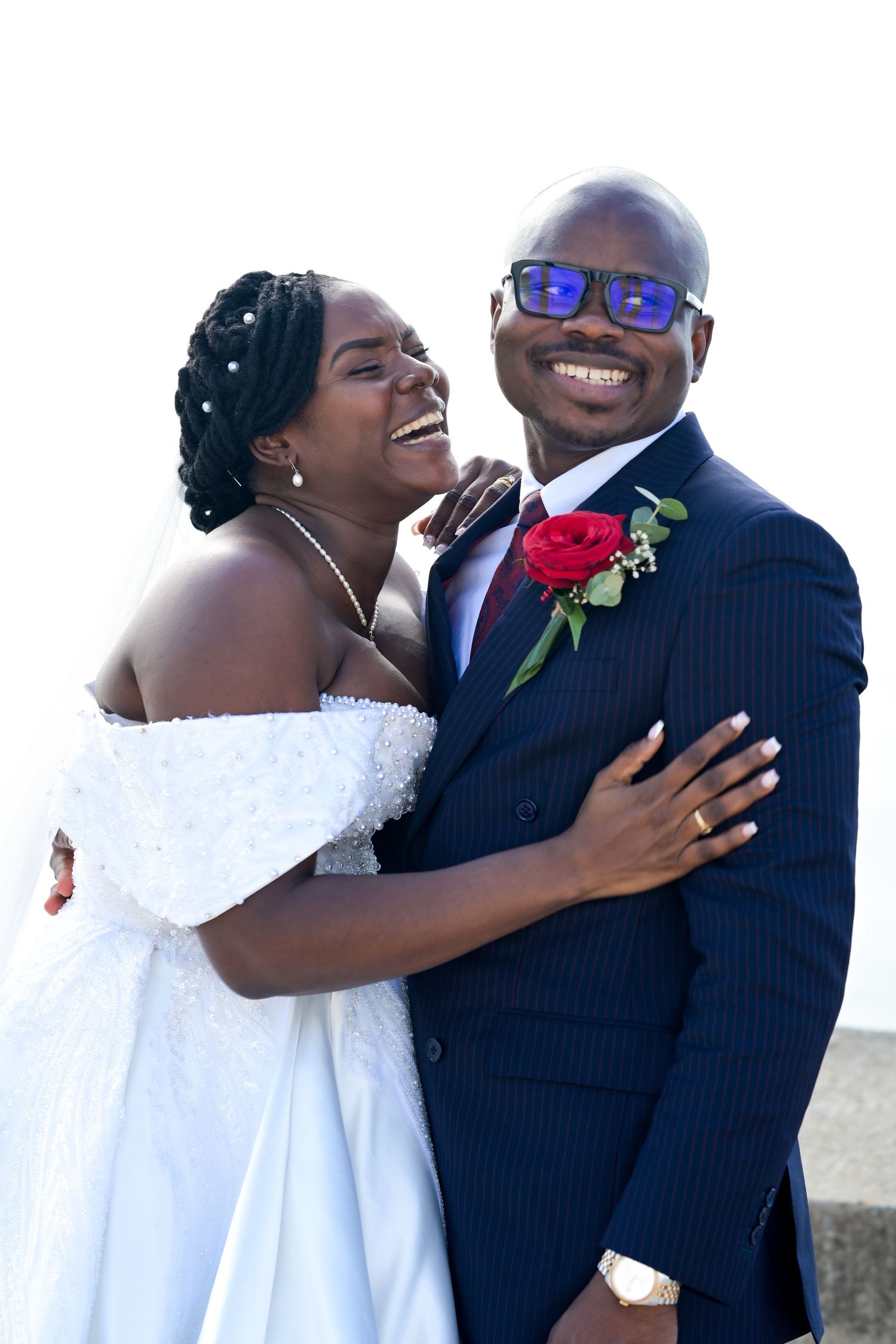 A joyful wedding couple embraces and laughs by the seaside.