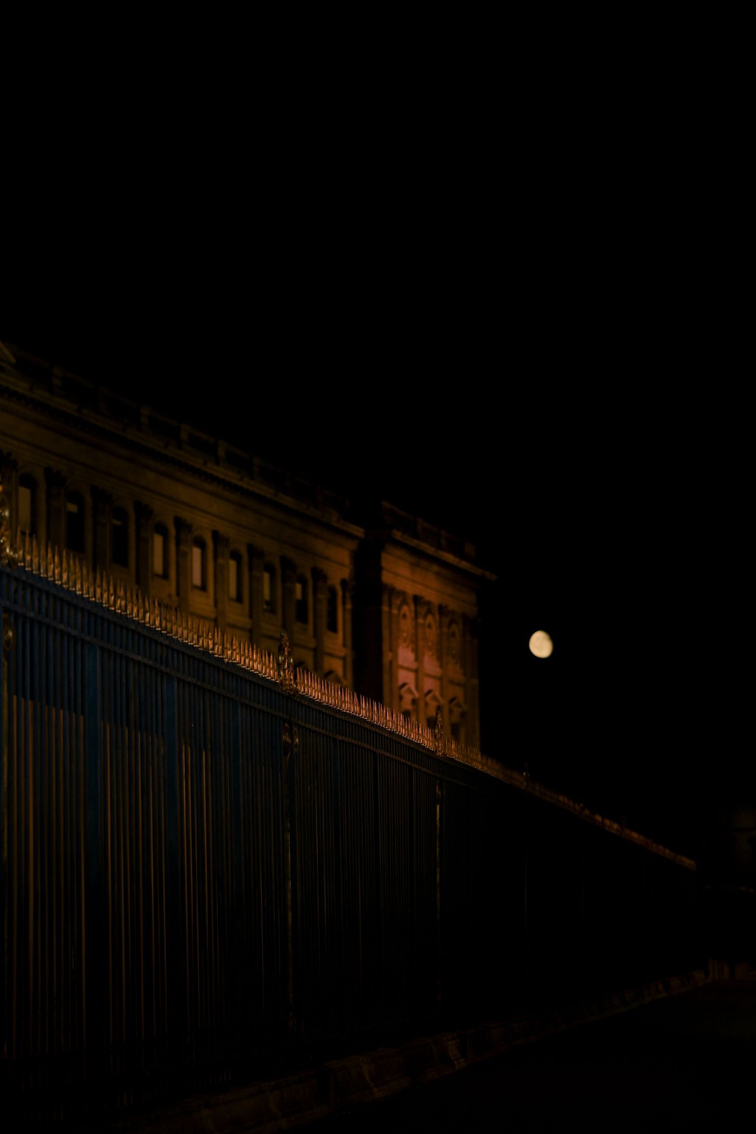 A moody architectural photo of an illuminated building facade with iron gates at night.