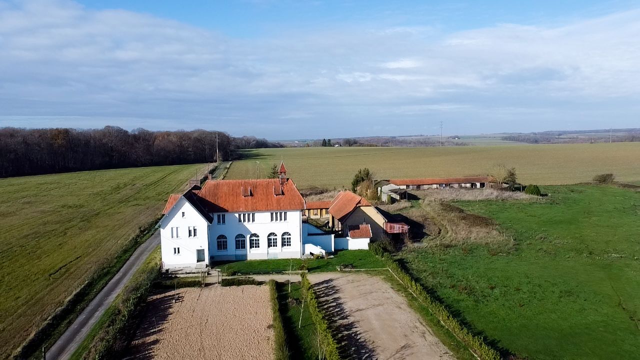 Aerial view of a white and blue house with red roof amid green rural landscape.