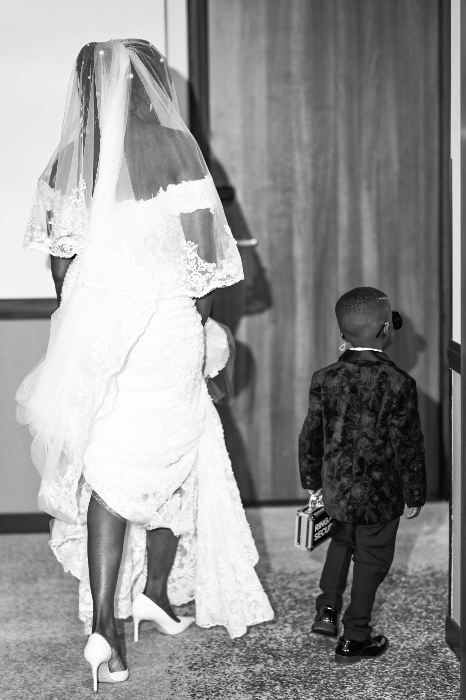 Black and white photo showing the bottom of a wedding dress and formal shoes.