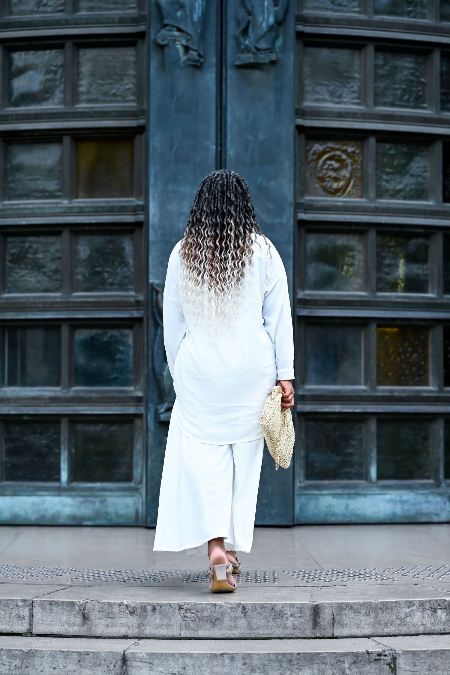 Person in white dress photographed against dark vintage building facade.