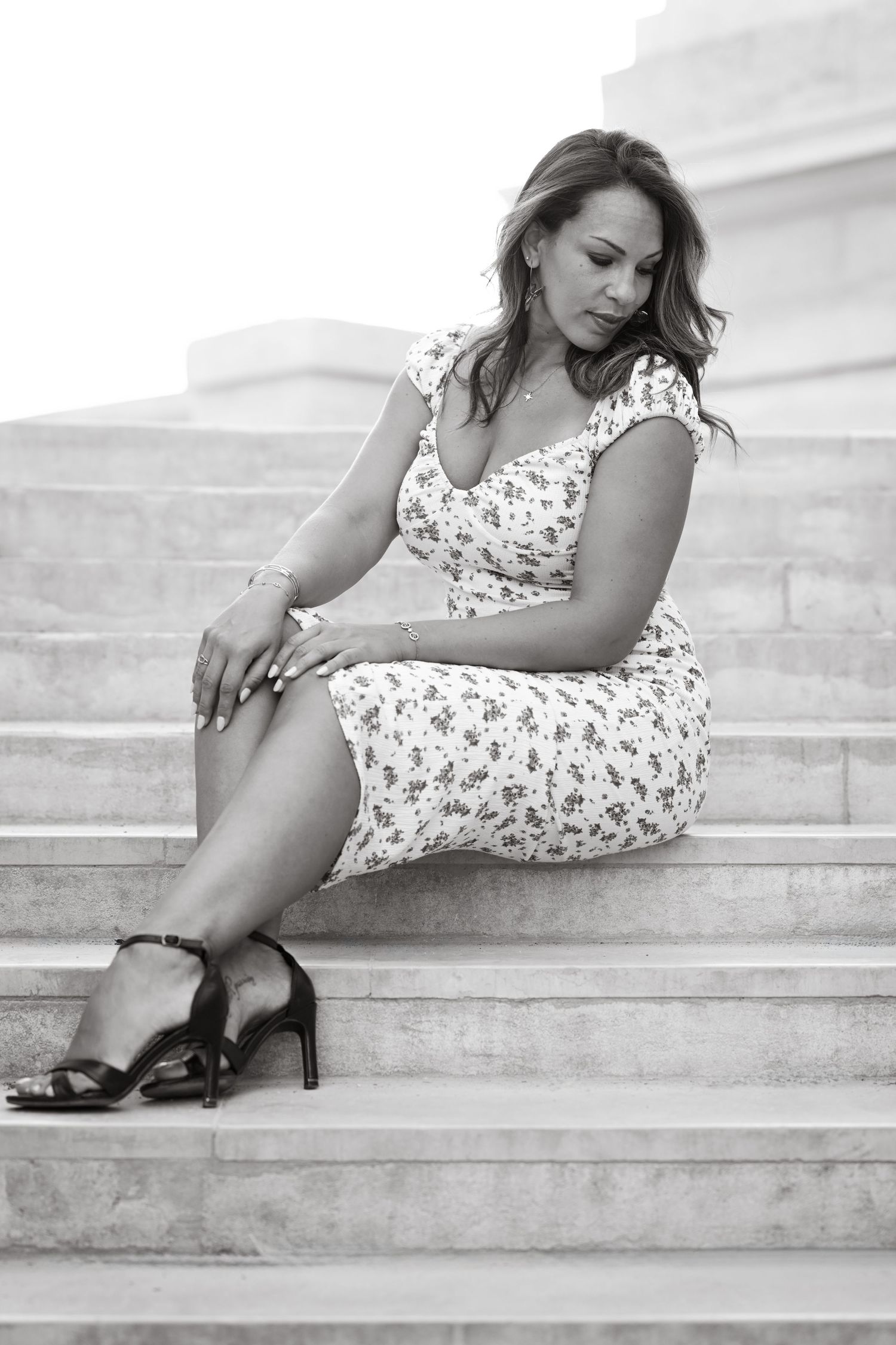 Black and white portrait of person in floral dress resting on stone steps.