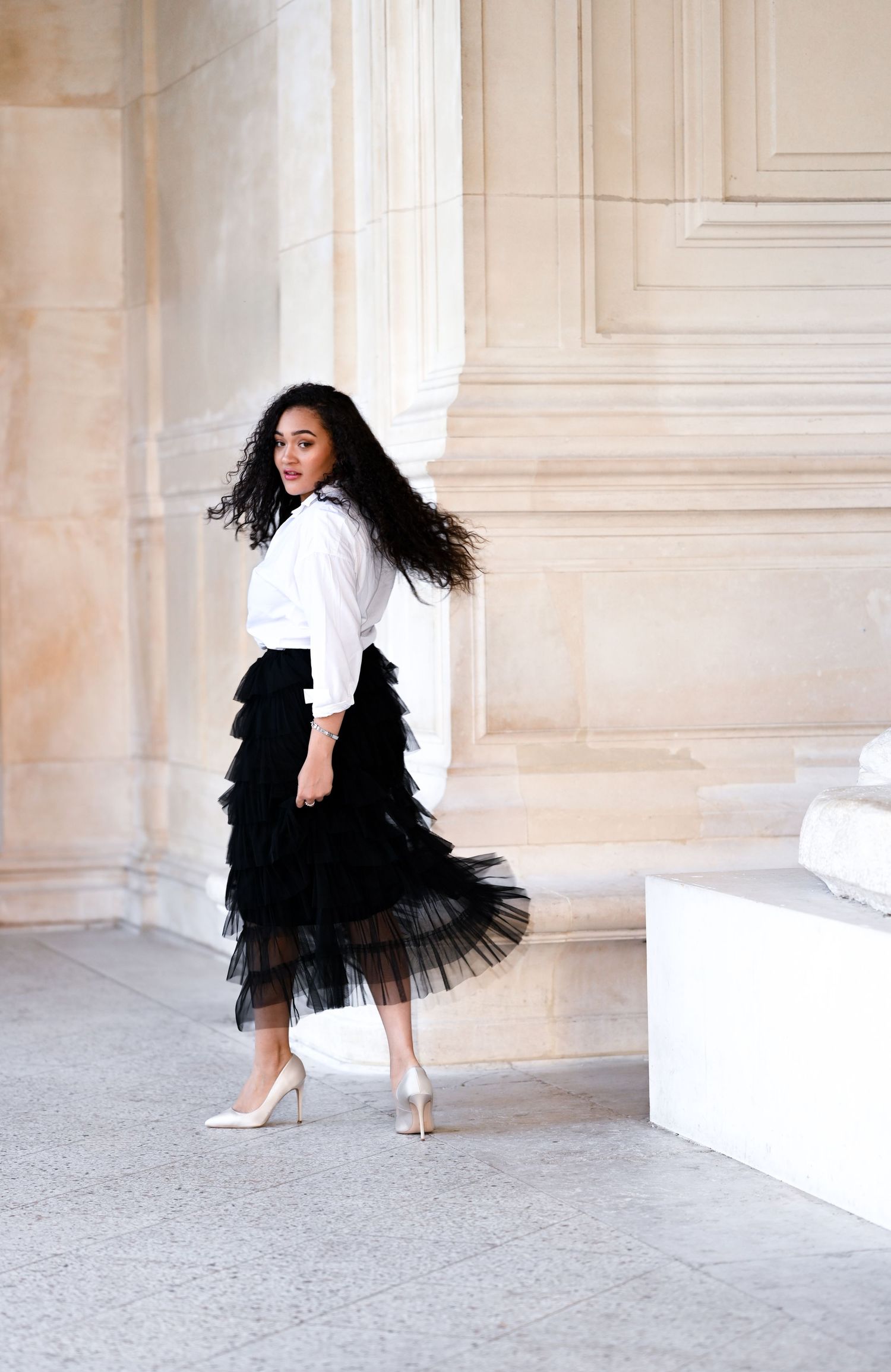 Figure in black tulle skirt poses dramatically against classical white stone colonnade.