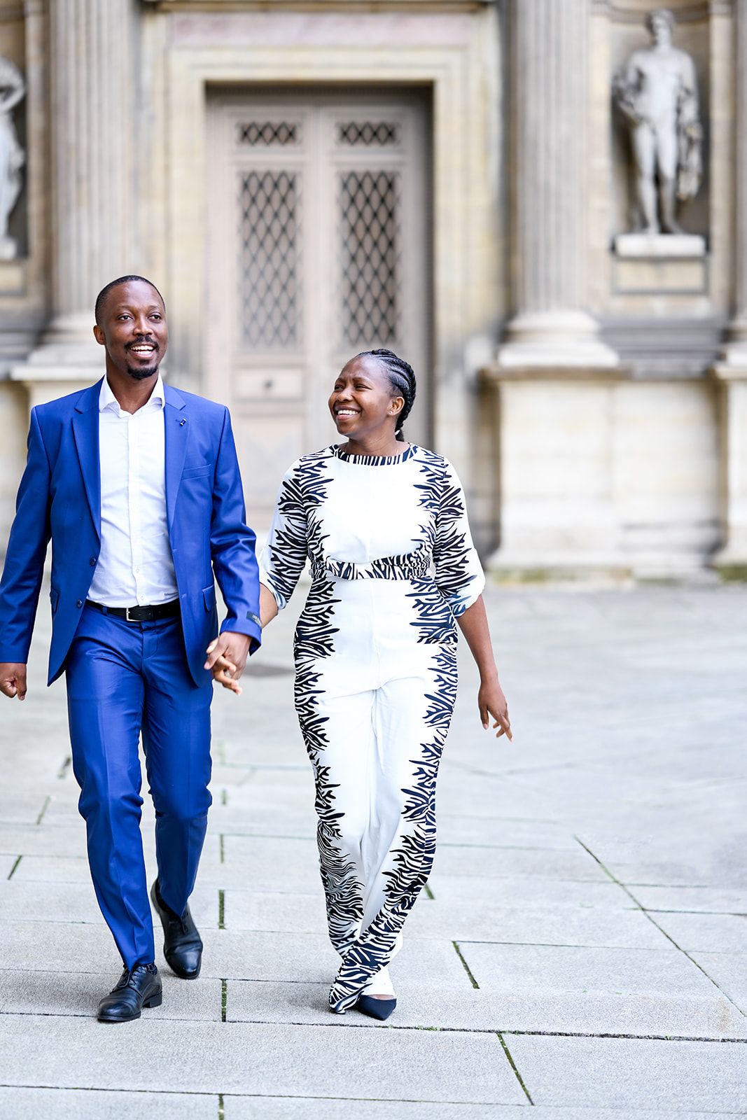 Two people share joyful moments while walking together near classical architecture.