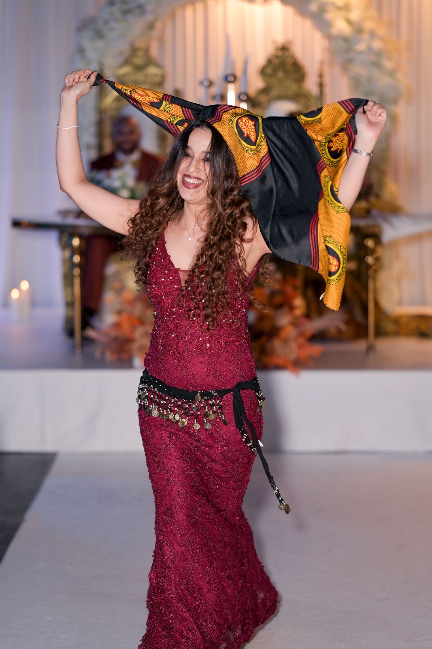 Woman in burgundy dress twirling and dancing with yellow fabric at formal event.