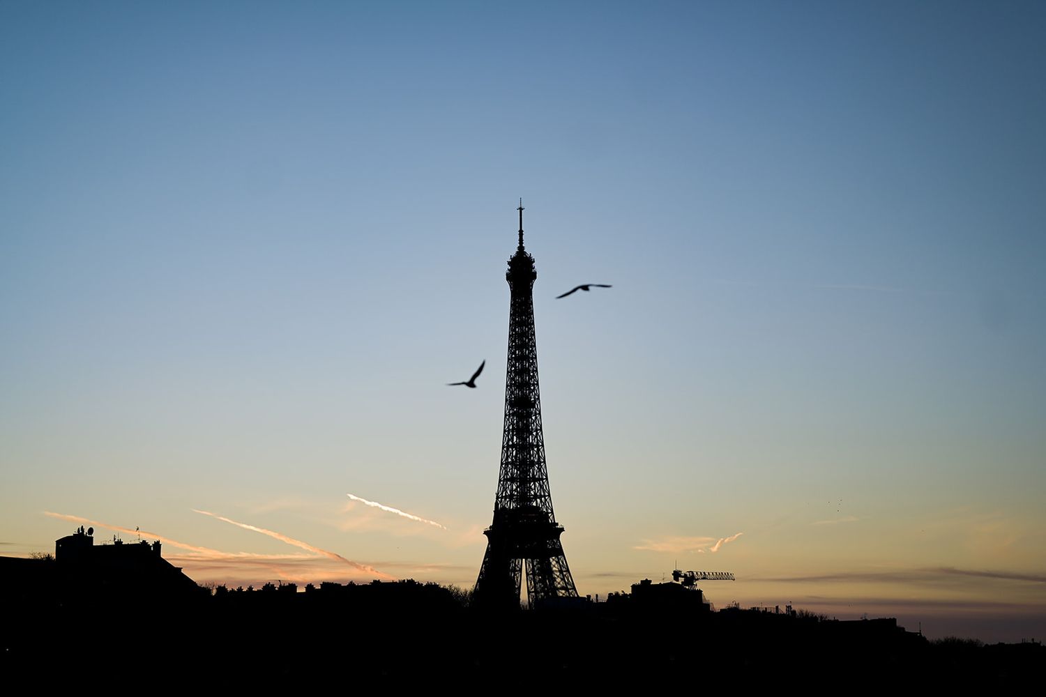 Silhouette of Paris skyline at sunset with Eiffel Tower visible against darkening blue sky.