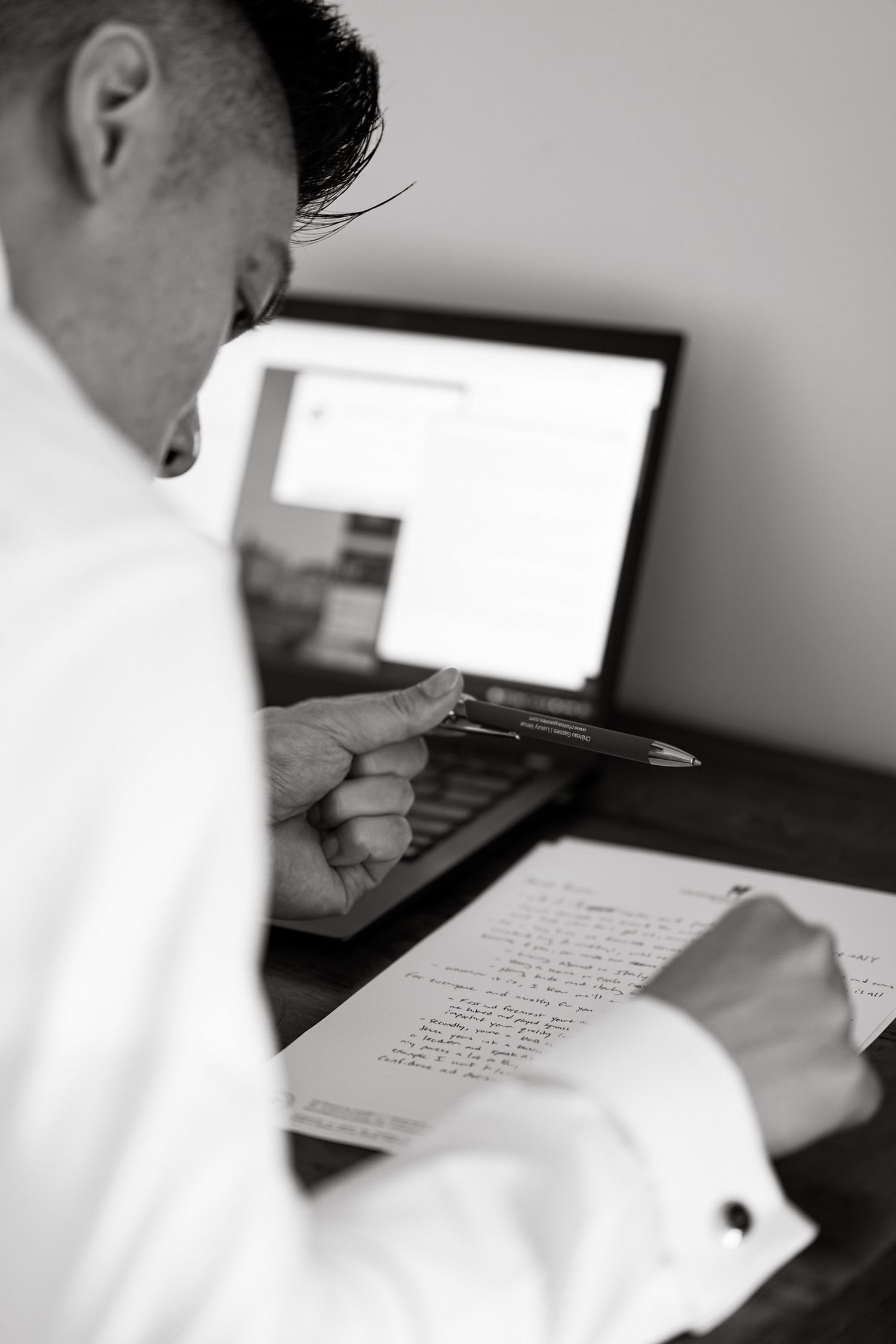 Person working at desk with laptop and documents in black and white.