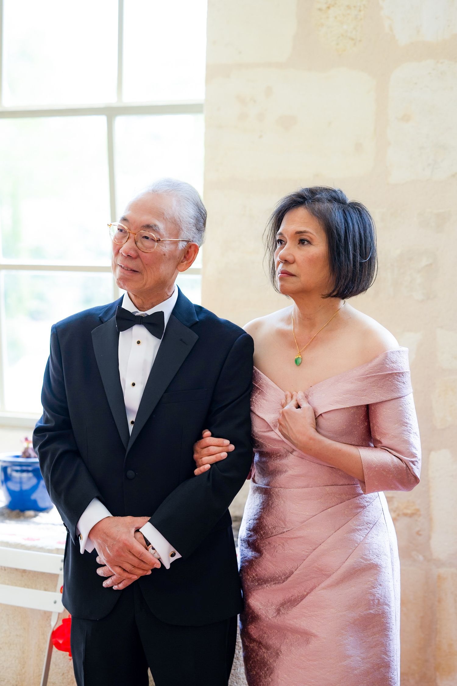 Formal portrait of two wedding guests in evening attire standing together indoors.