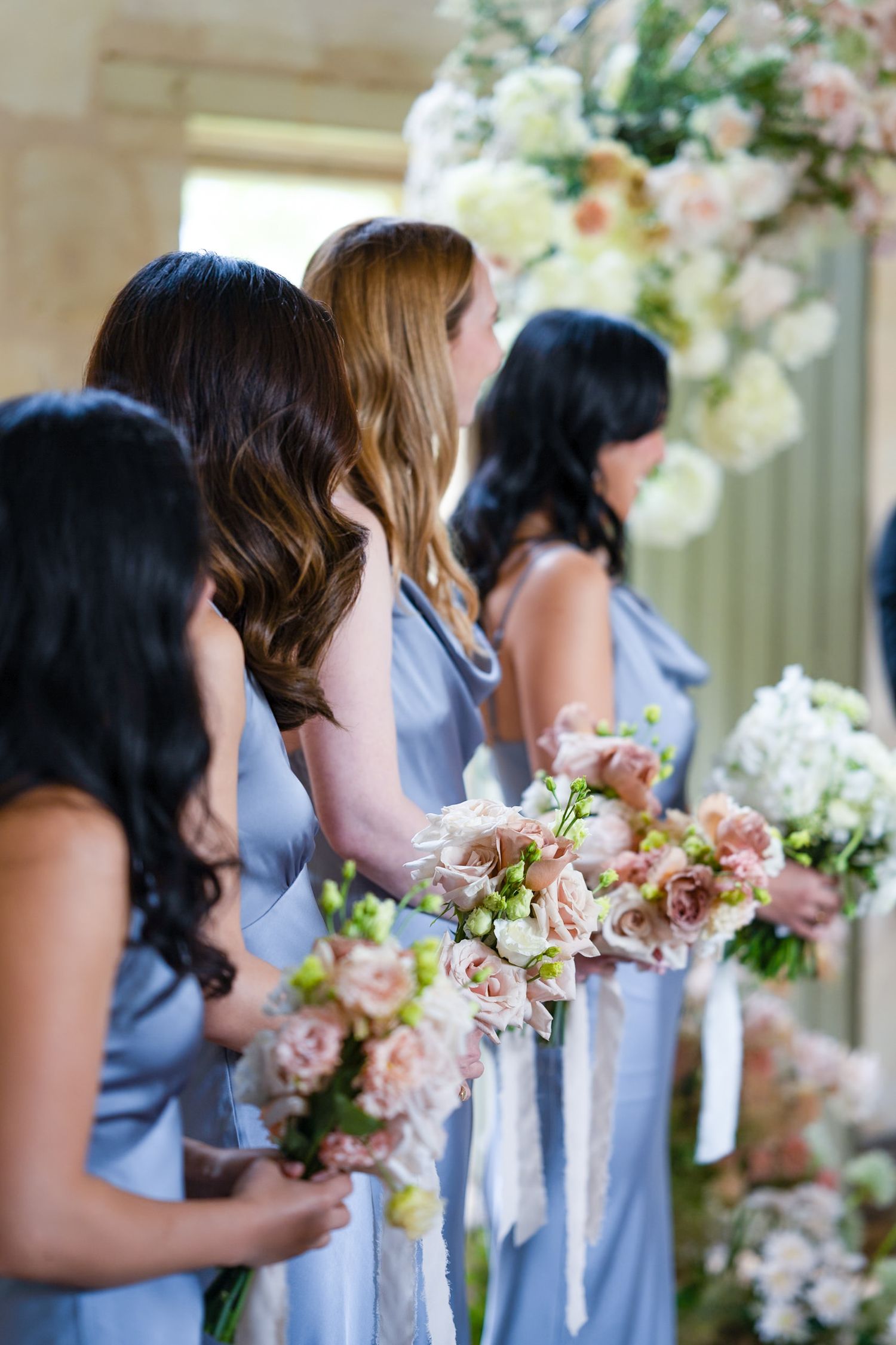Bridesmaids in light blue dresses hold pink and white bouquets.