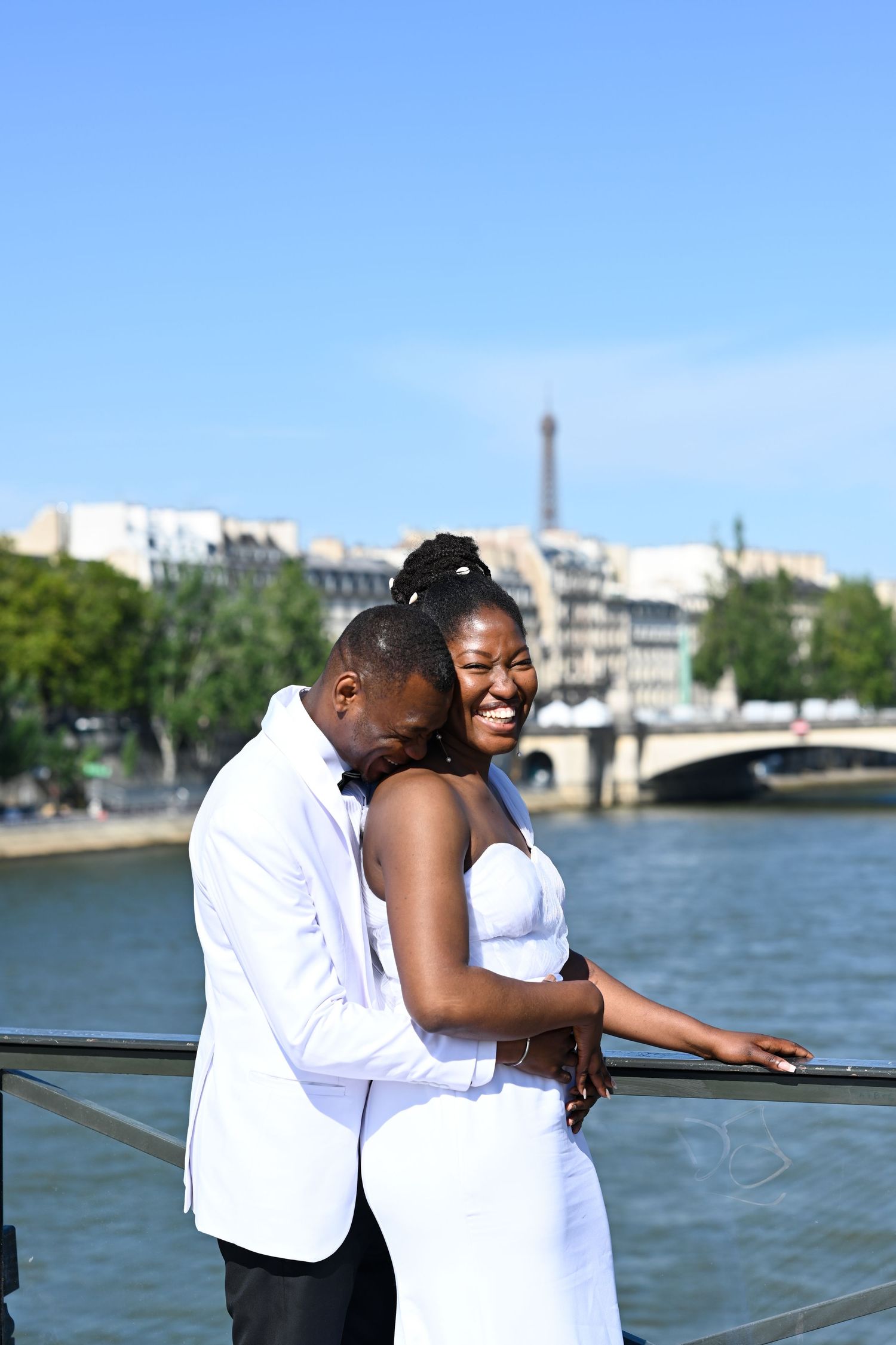 A romantic moment captured along the Seine River in Paris with city views in the background.
