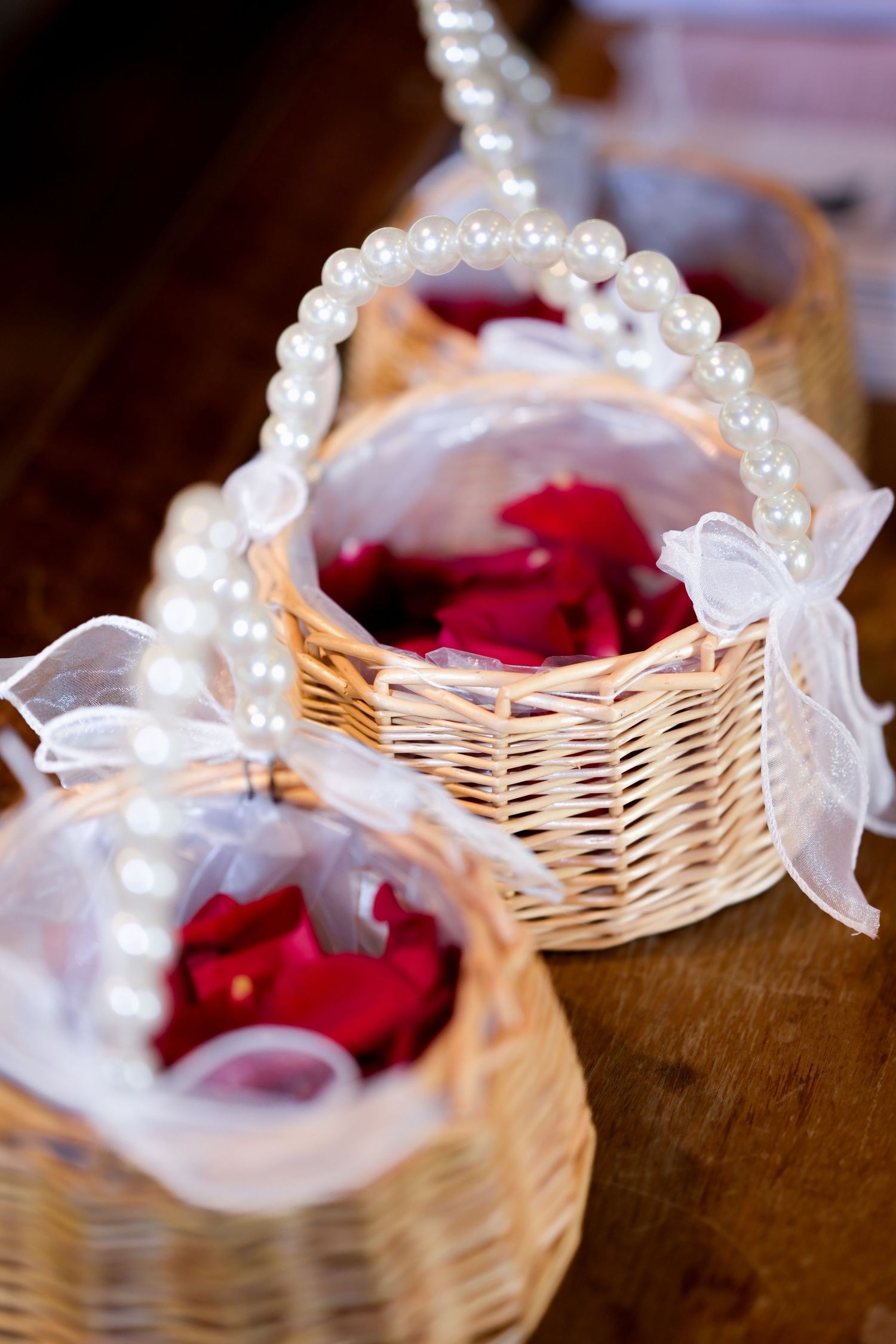Wicker basket decorated with pearls and ribbons containing red rose petals.
