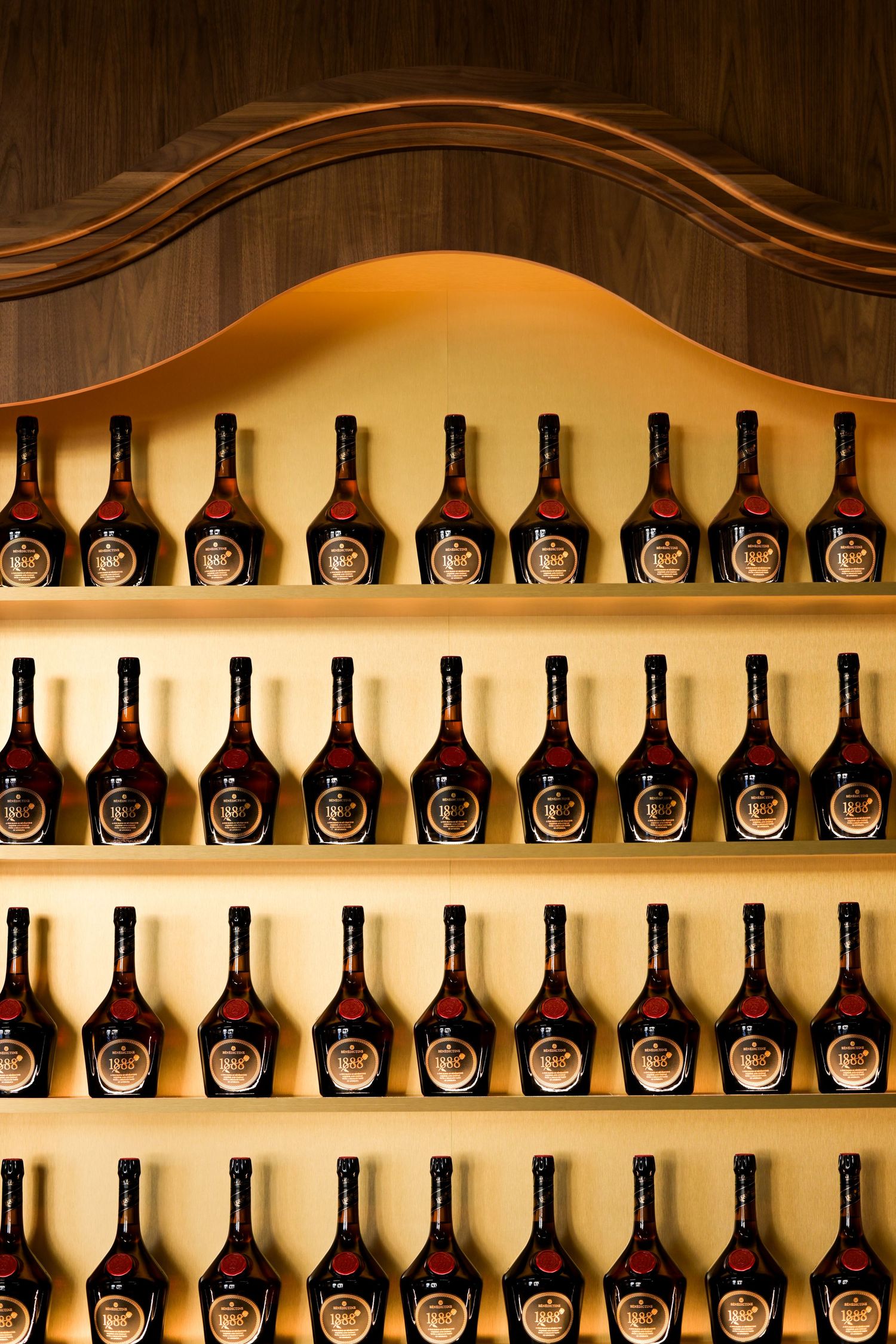 Rows of identical dark bottles arranged on illuminated wooden shelves in what appears to be a wine cellar or display.