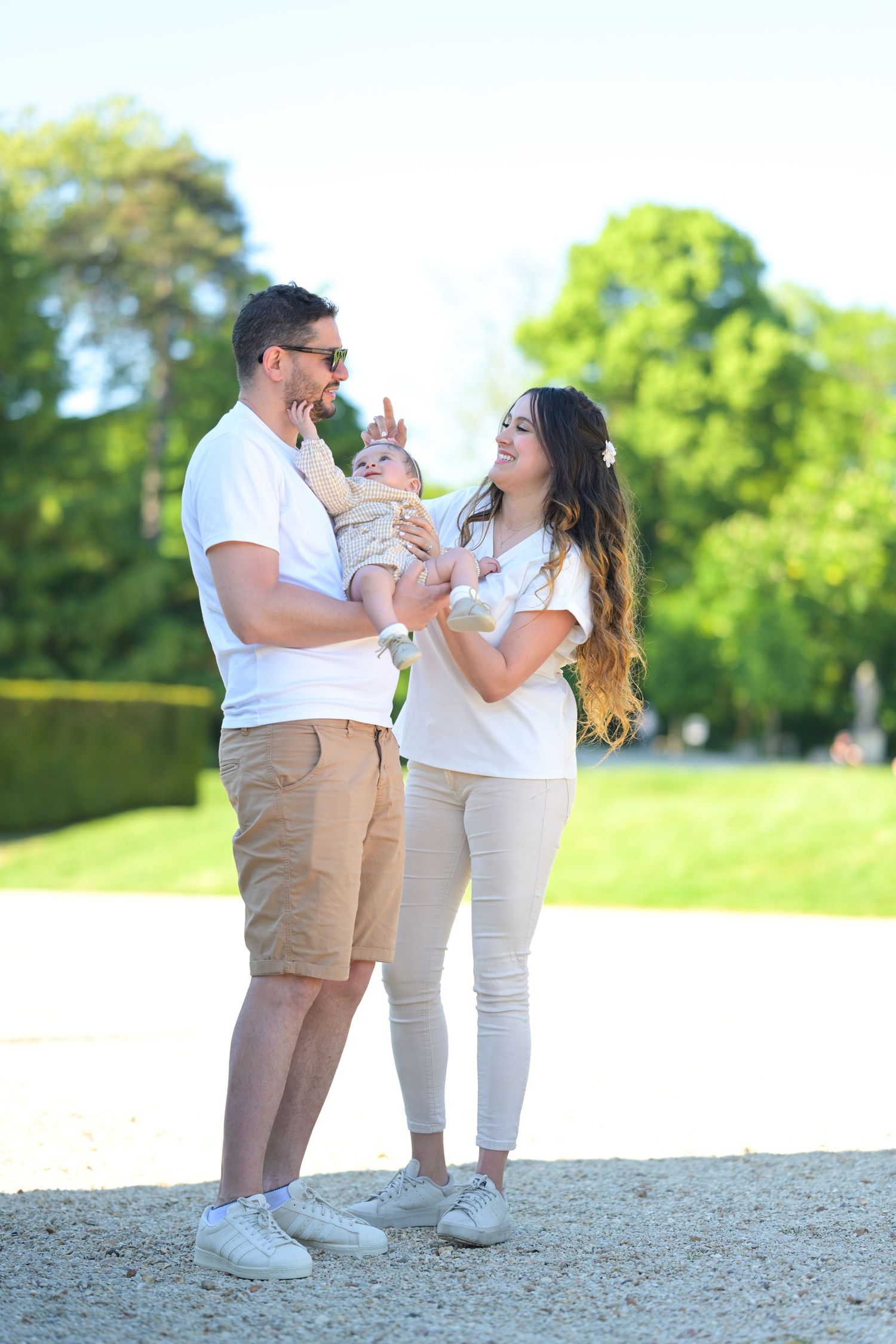 Three people in matching outfits share a tender moment on a gravel path with green trees in background.
