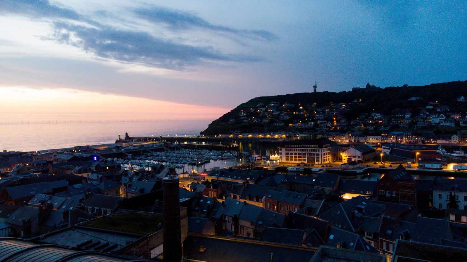 Aerial view of Whitby town at dusk with illuminated buildings and harbor beneath cloudy twilight sky.