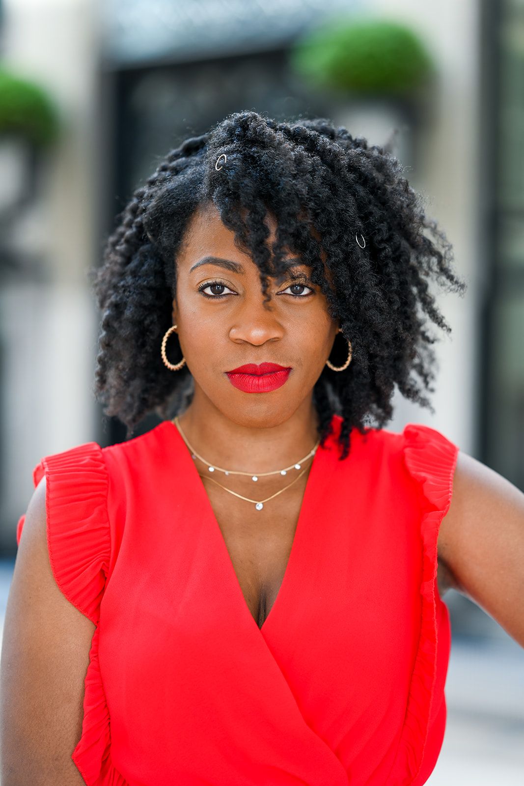 A close-up fashion portrait showcasing a red sleeveless top with ruffled details and gold jewelry.
