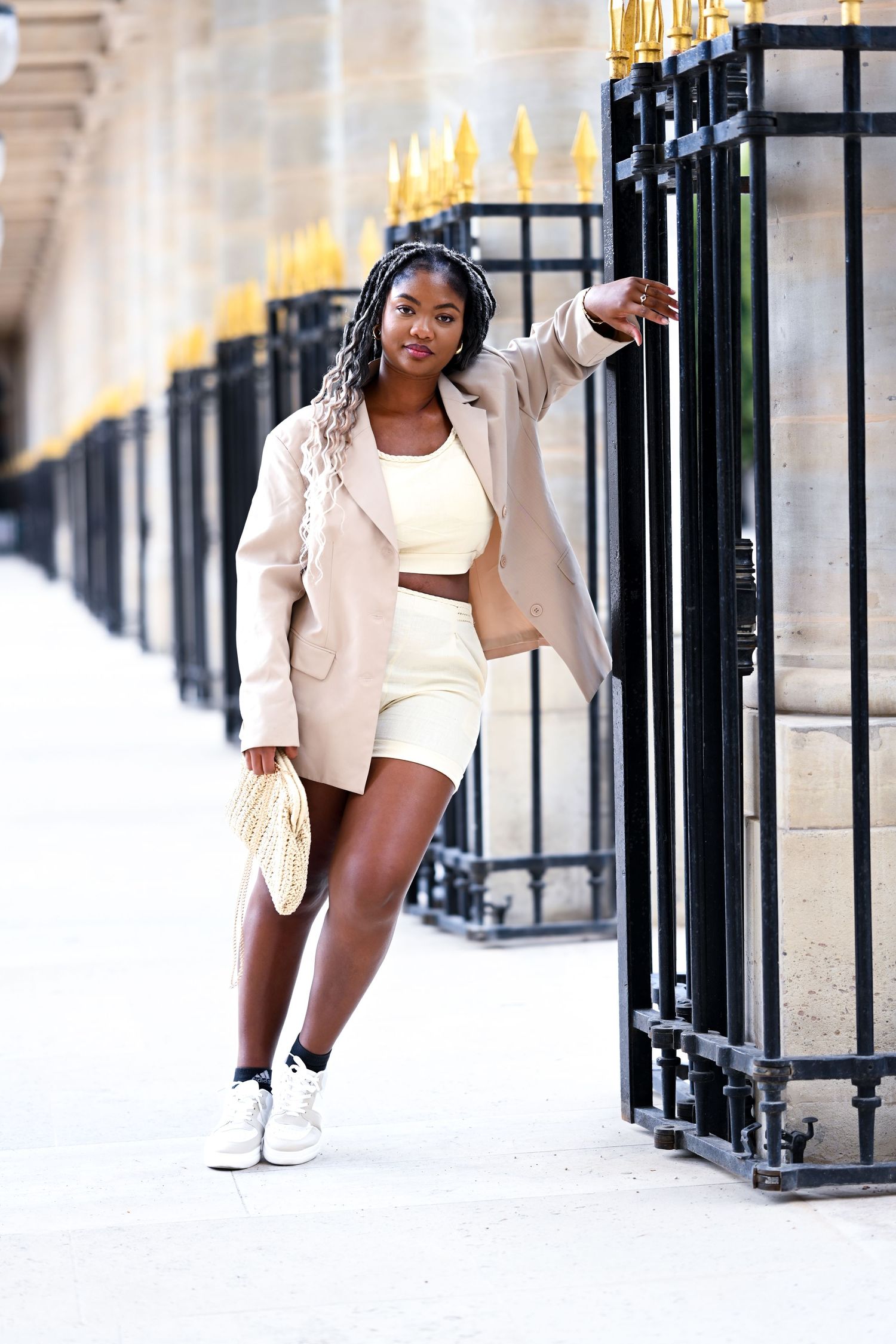 Fashion model poses in cream colored blazer and white outfit against ornate architectural backdrop.