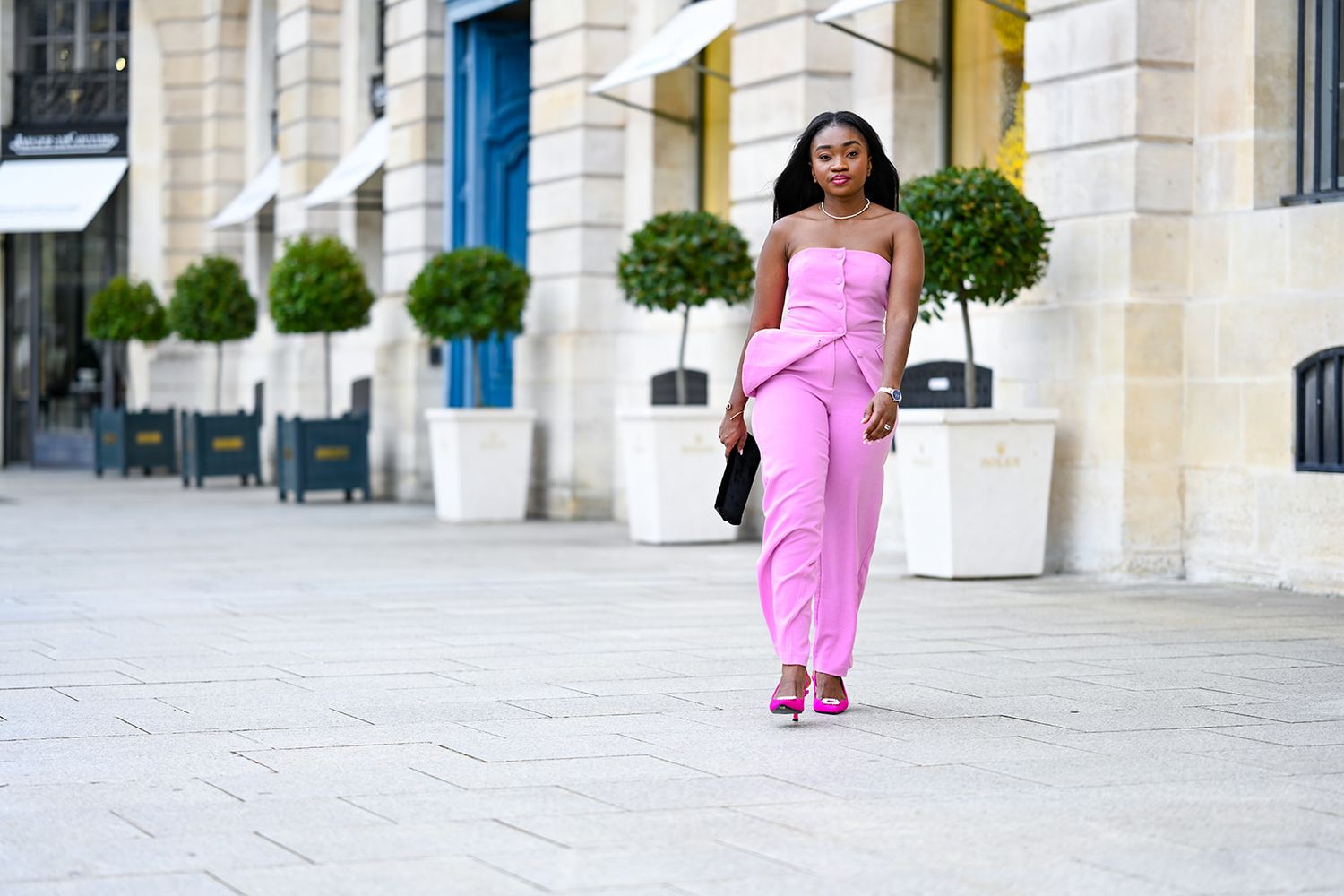 Stylish pink jumpsuit outfit photographed in front of elegant building with manicured topiaries.