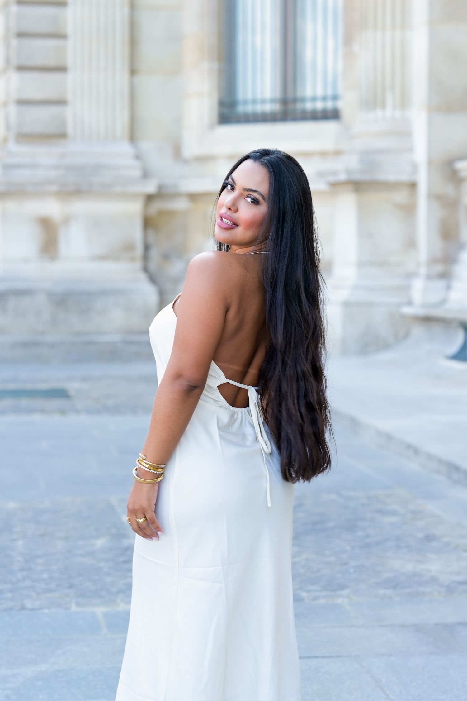 Fashion model in white dress showcases playful poses against architectural backdrop.