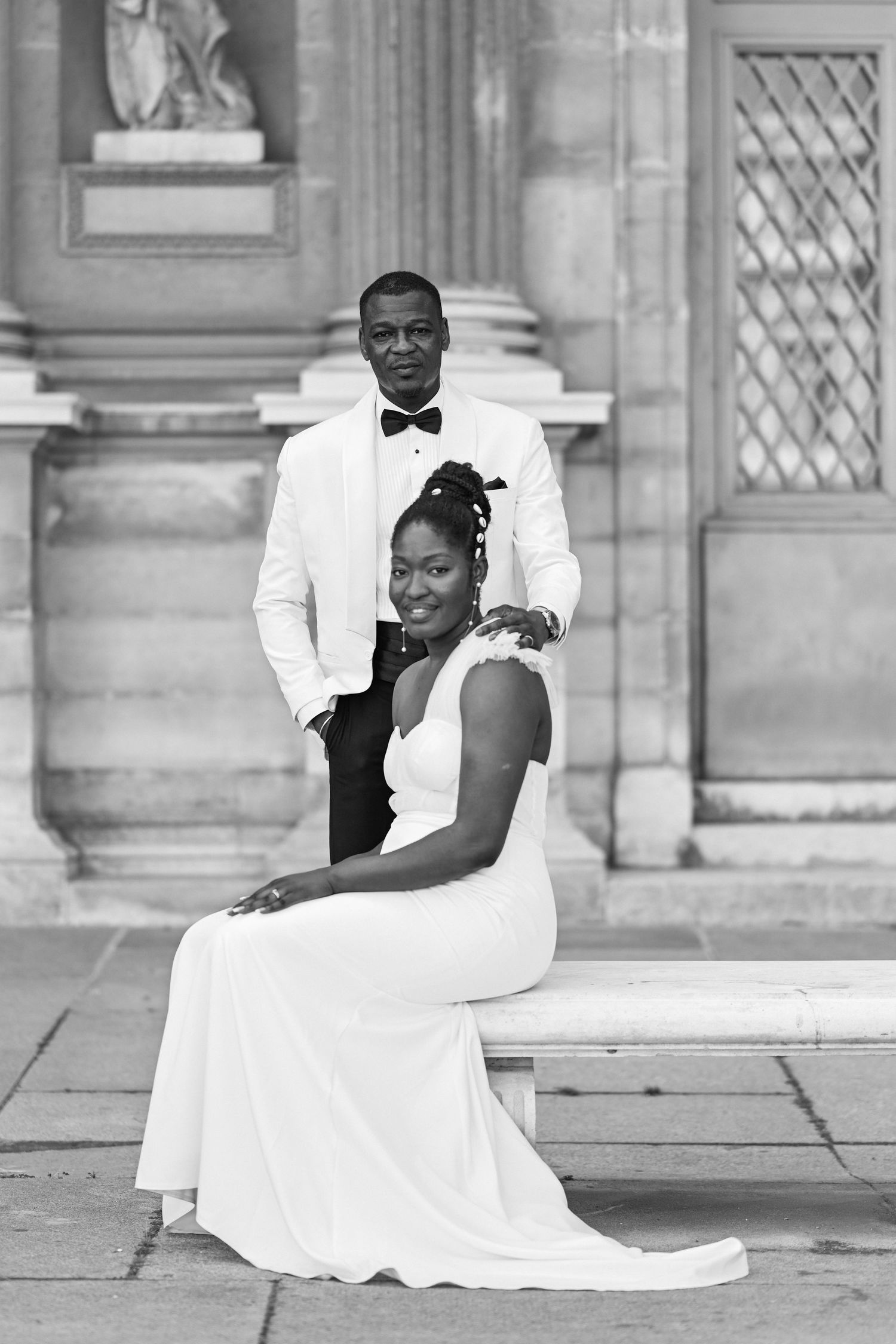 Elegant wedding portrait of couple in white attire against classical architecture.