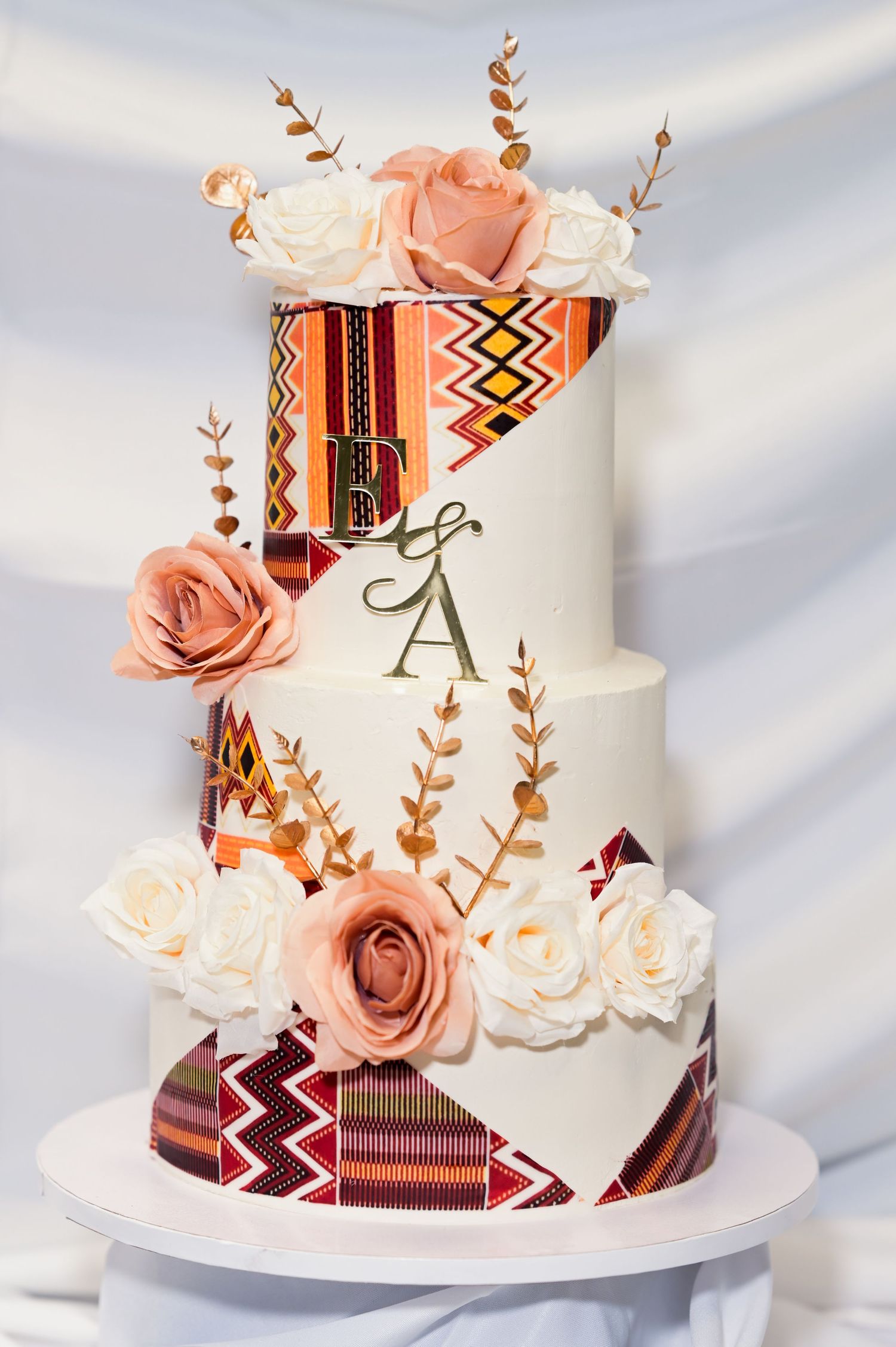 Elegant white wedding cake decorated with peach roses and geometric African print details.